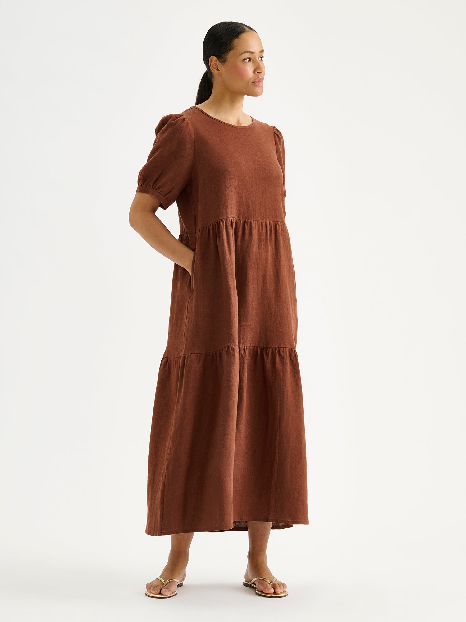 The Sarastus long brown linen dress with voluminous frill layers and short puff sleeves on a model
