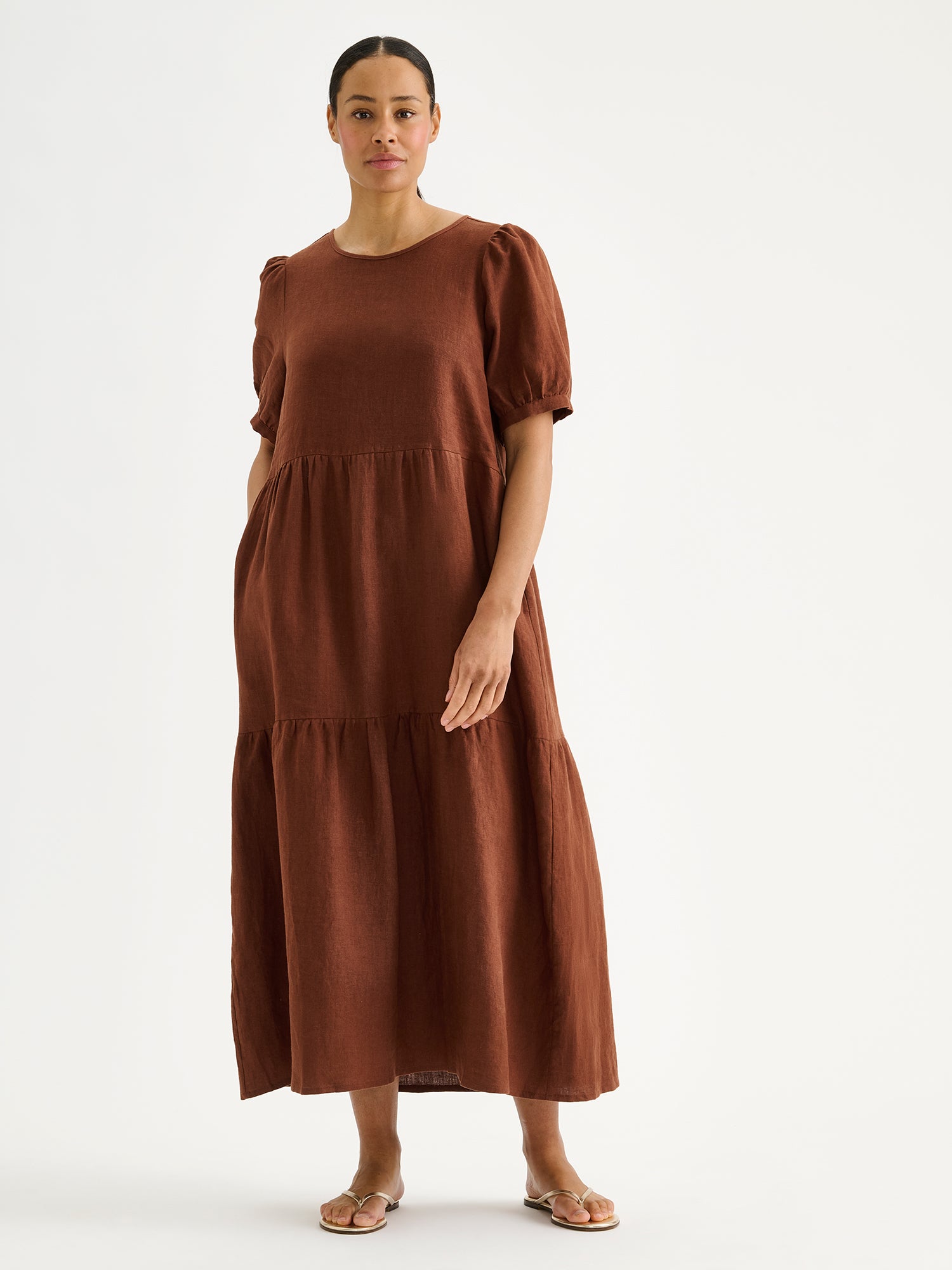 The Sarastus long brown linen dress with voluminous frill layers and short puff sleeves on a model