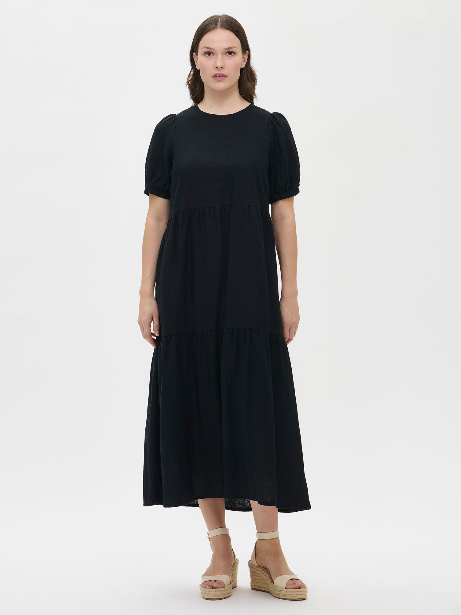 The Sarastus long black dress for women is made of high-quality, durable, and breathable woven linen fabric. With its voluminous frill layers and short puff sleeves, this dress exudes both elegance and comfort. Worn by a model in size S from the front.