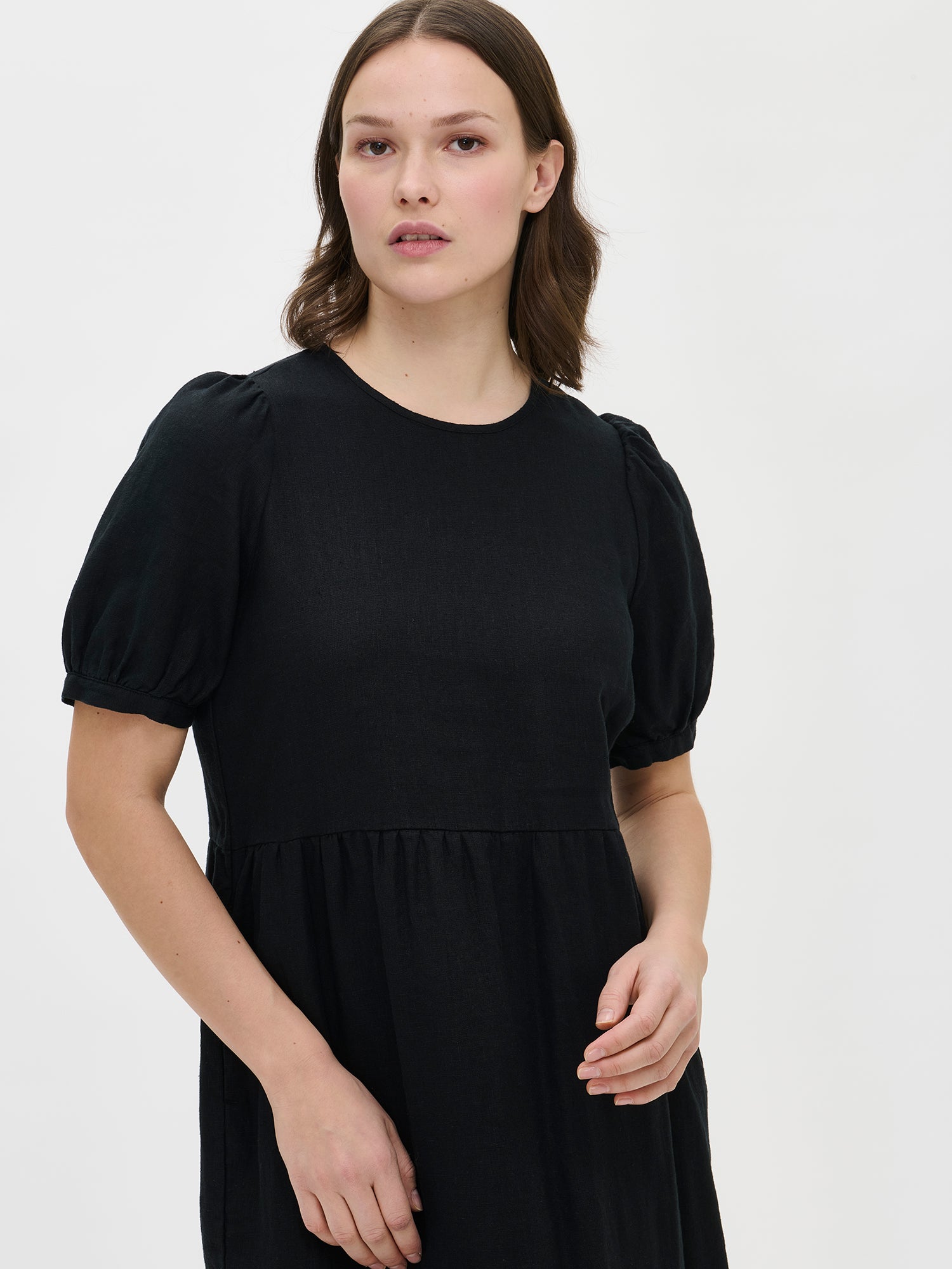 The Sarastus long black dress for women is made of high-quality, durable, and breathable woven linen fabric. With its voluminous frill layers and short puff sleeves, this dress exudes both elegance and comfort. Worn by a model in size S from the front.