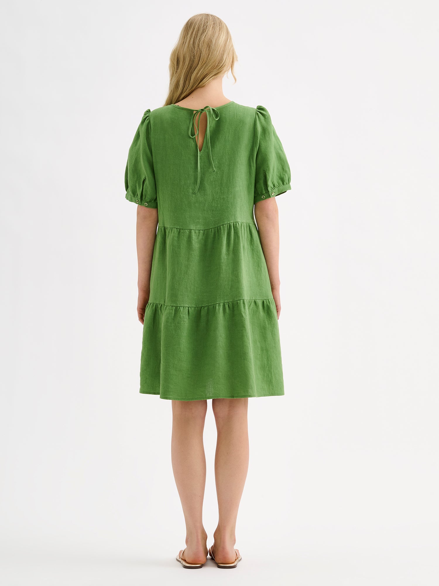 Nanso women's beautiful green Sarastus linen dress with voluminous frill layers and short puff sleeves on a model with sandals, pictured from the backside