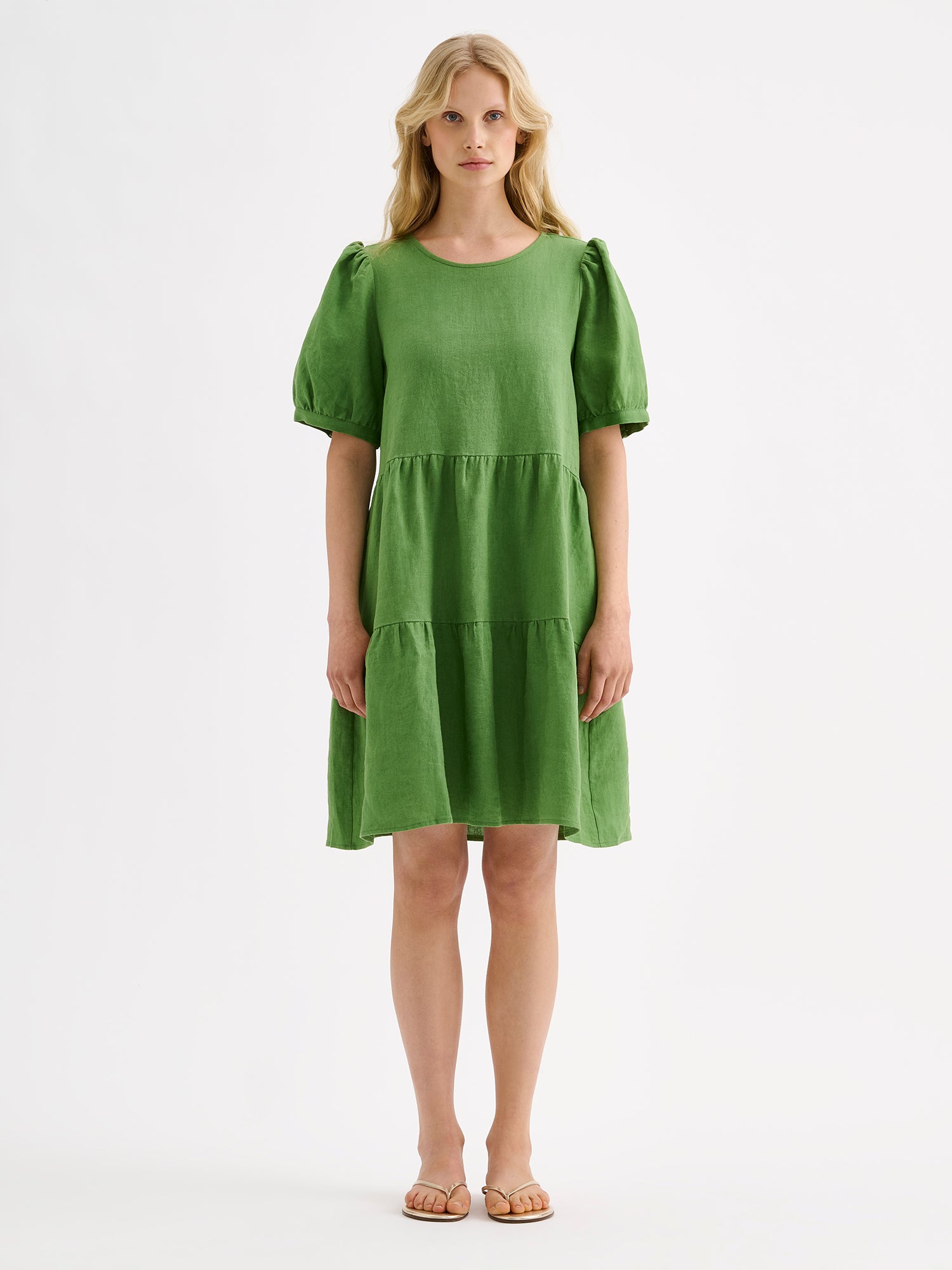 Nanso women's beautiful green Sarastus linen dress with voluminous frill layers and short puff sleeves on a model with sandals.