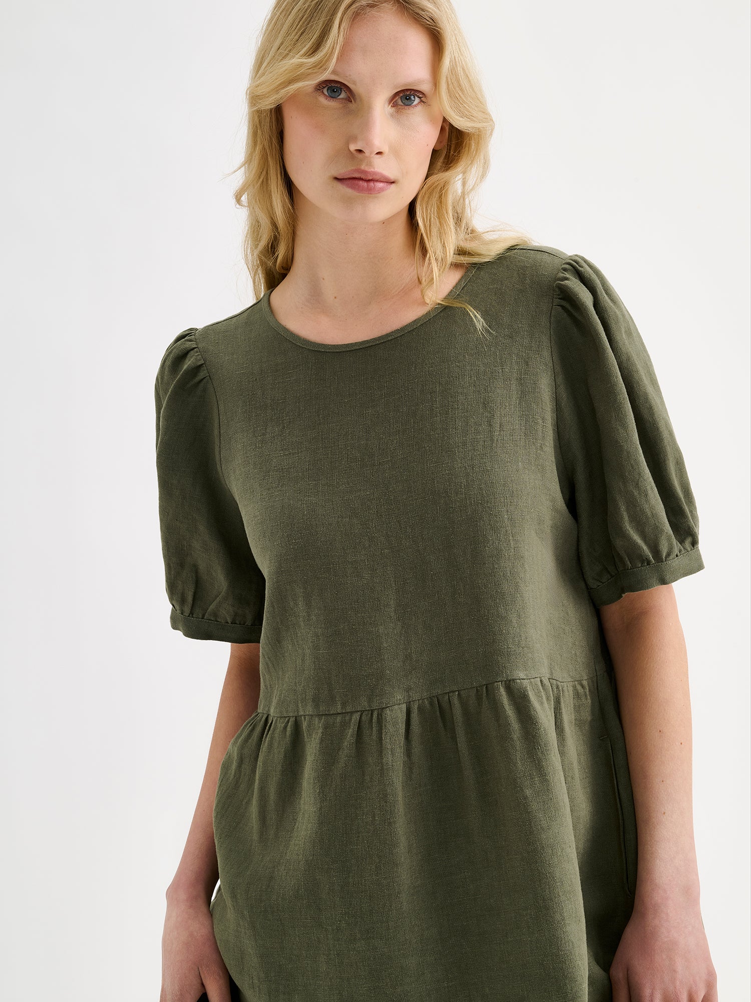 Nanso women's beautiful olive green Sarastus linen dress with voluminous frill layers and short puff sleeves on a blonde model, closeup.