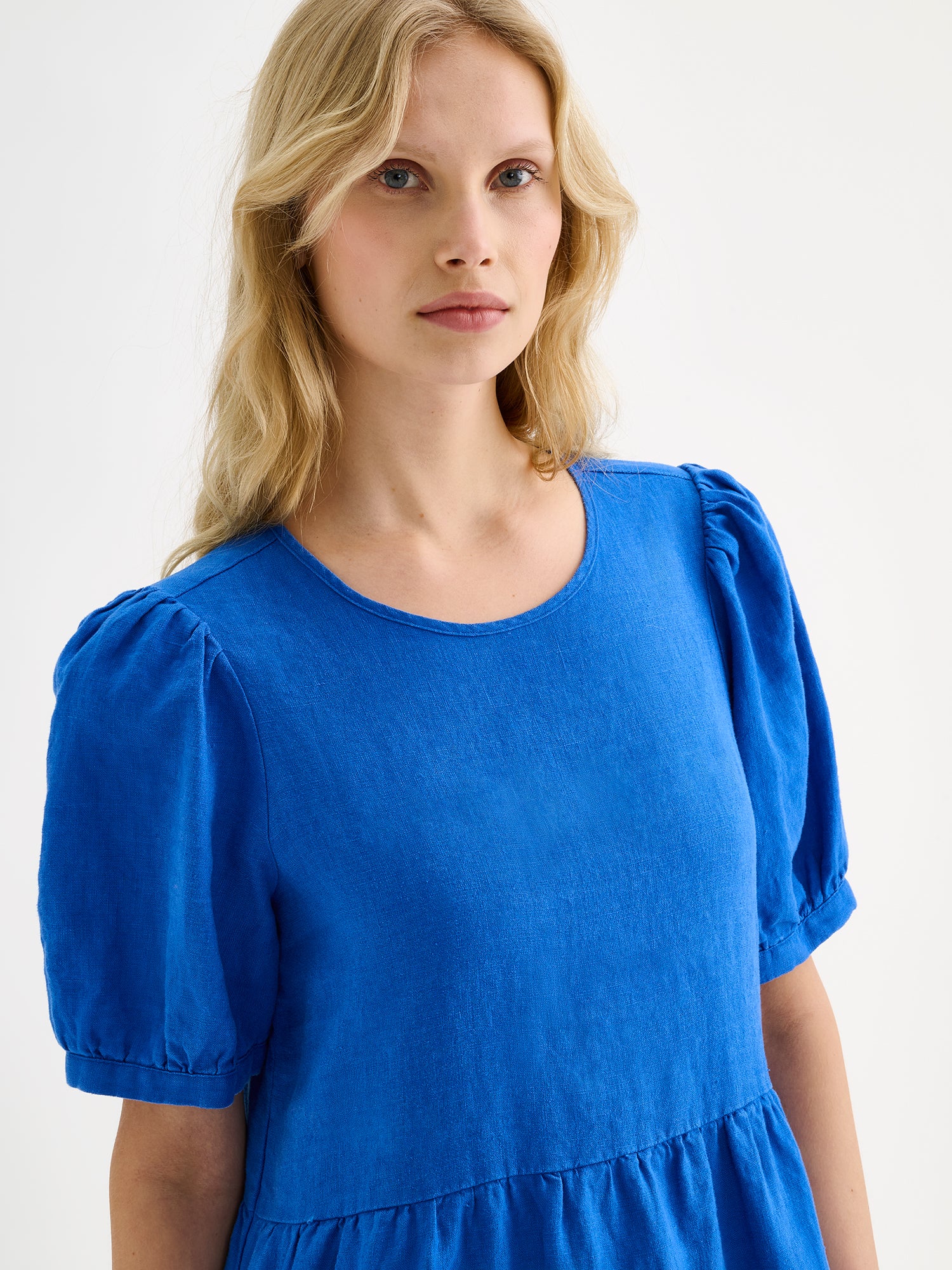 Nanso women's beautiful blue Sarastus linen dress with voluminous frill layers and short puff sleeves, on a model, close-up.