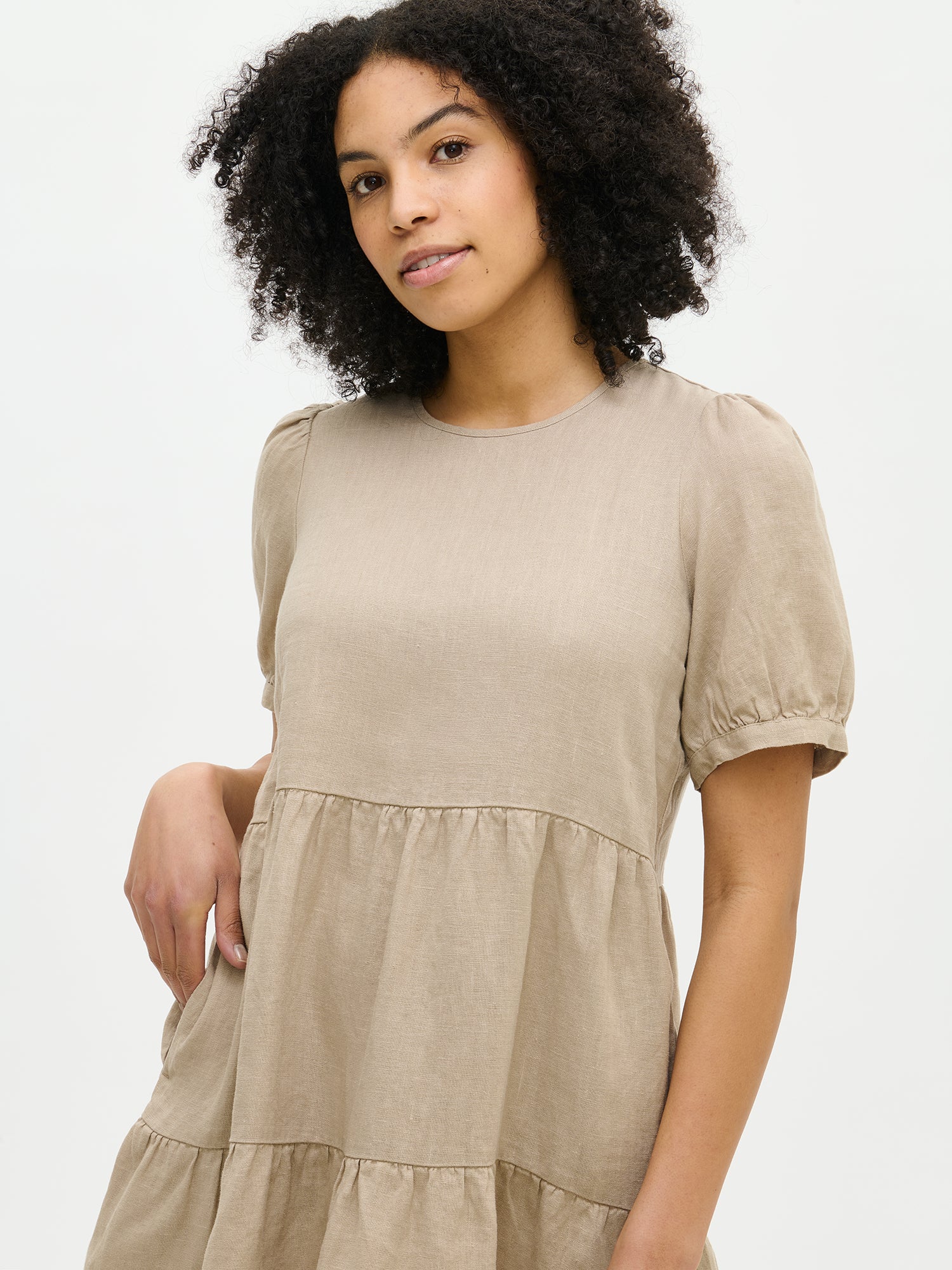 Nanso women's beautiful beige Sarastus linen dress with voluminous frill layers and short puff sleeves, image taken on the model from the front close-up.