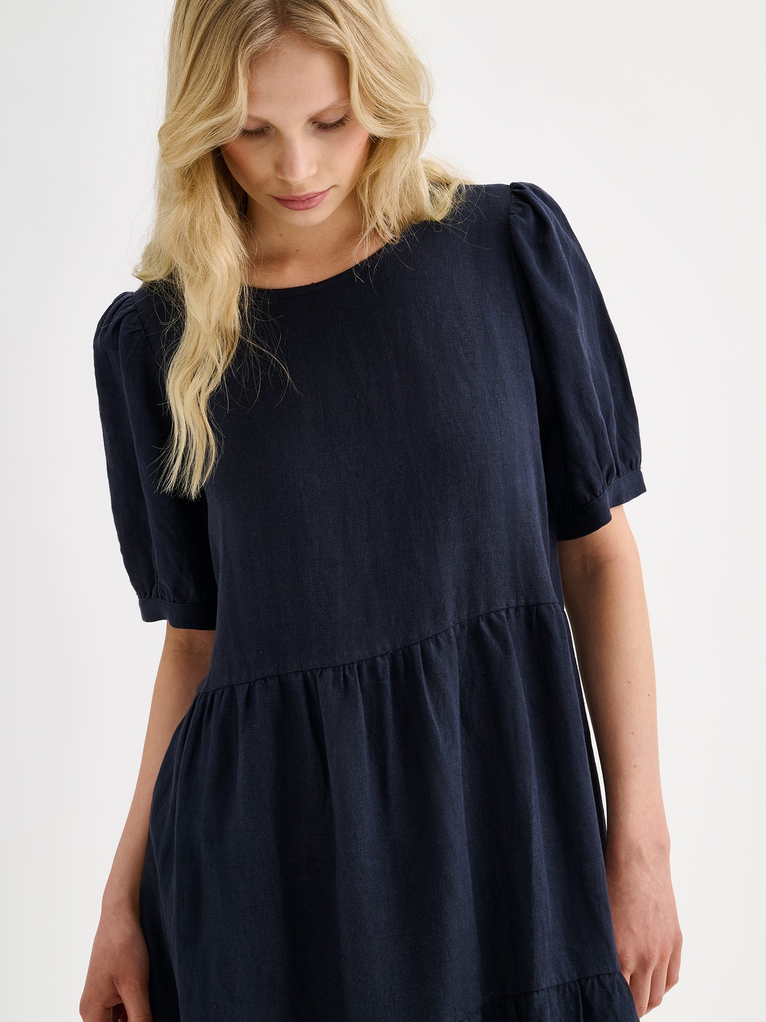 Nanso women's beautiful dark blue Sarastus midi linen dress features voluminous frill layers and short puff sleeves on a model, close-up.
