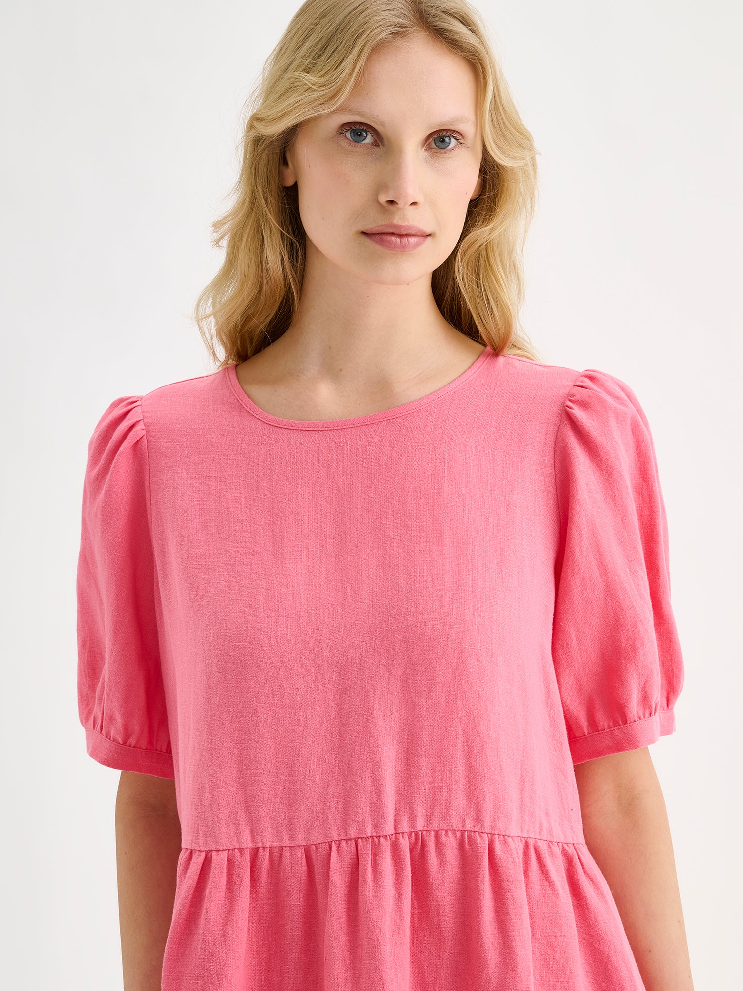 Nanso women's beautiful pink Sarastus midi linen dress features voluminous frill layers and short puff sleeves. This stylish summer dress is made of high-quality linen. Pictured on a blonde model, close-up.