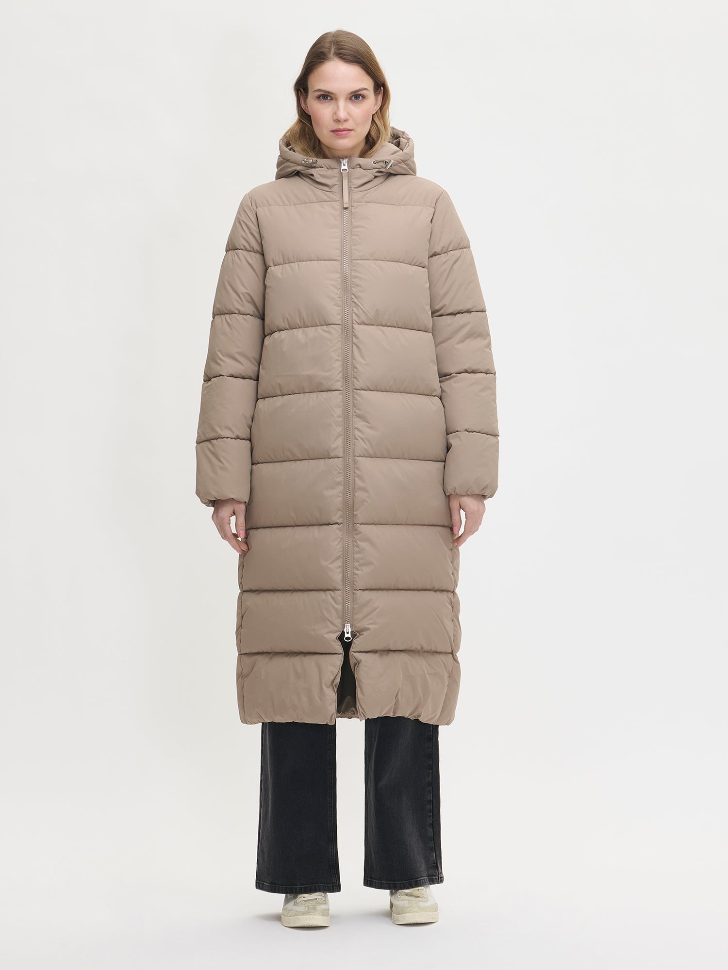 The Lumi Long Pink Puffer Coat in beige offers cozy warmth with its lightweight, puffy insulation. Worn by a model in size S.