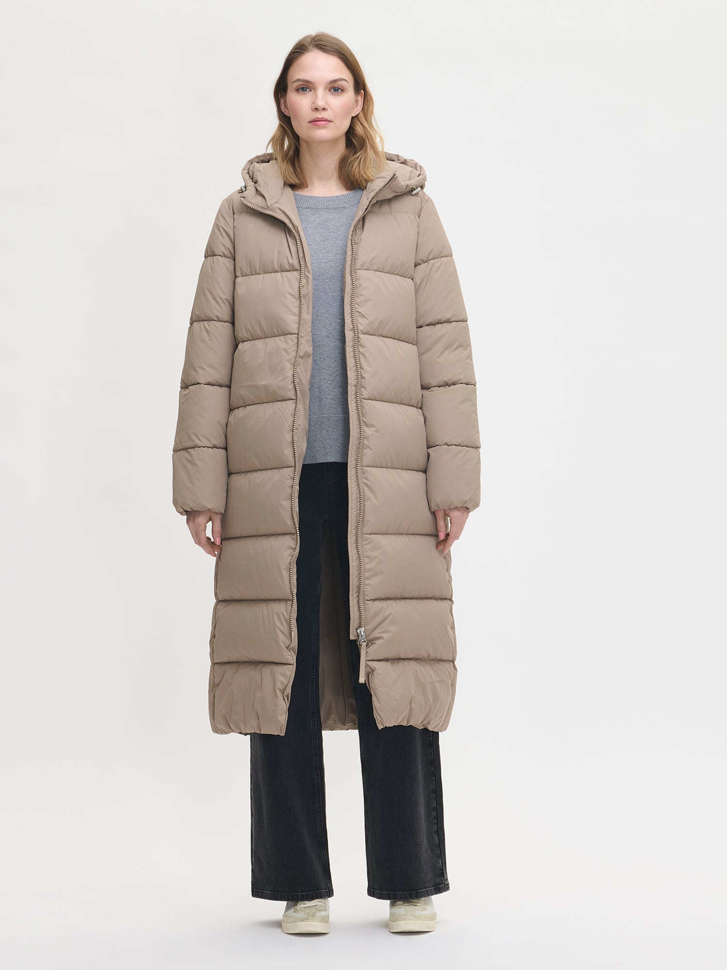 The Lumi Long Pink Puffer Coat in beige offers cozy warmth with its lightweight, puffy insulation. Worn by a model and jacket open.