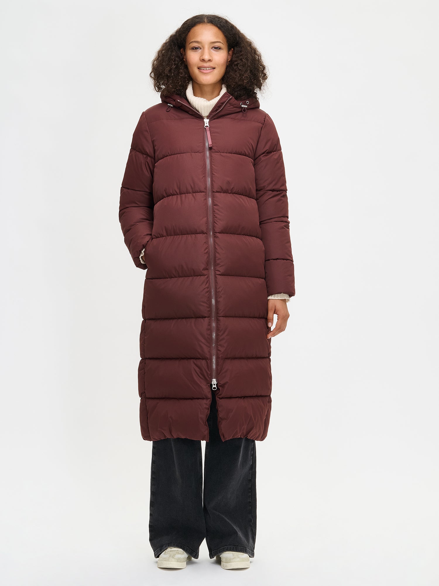 The Lumi Long Pink Puffer Coat in beige offers cozy warmth with its lightweight, puffy insulation. Worn by a model in size S.