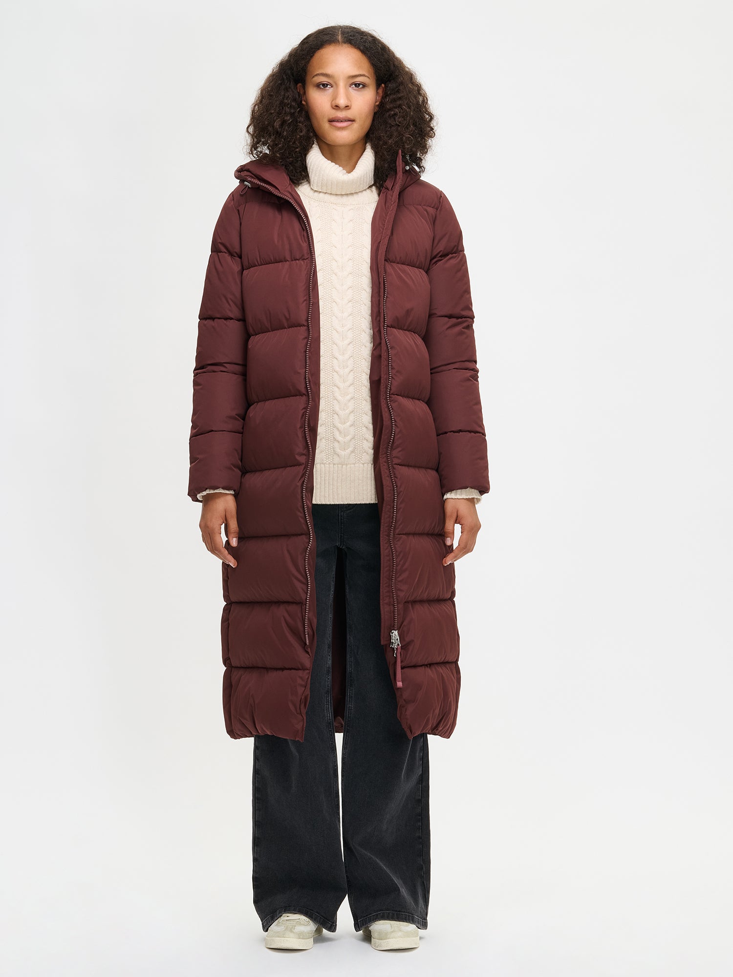 The Lumi Long Pink Puffer Coat in beige offers cozy warmth with its lightweight, puffy insulation. Worn by a model and jacket open.