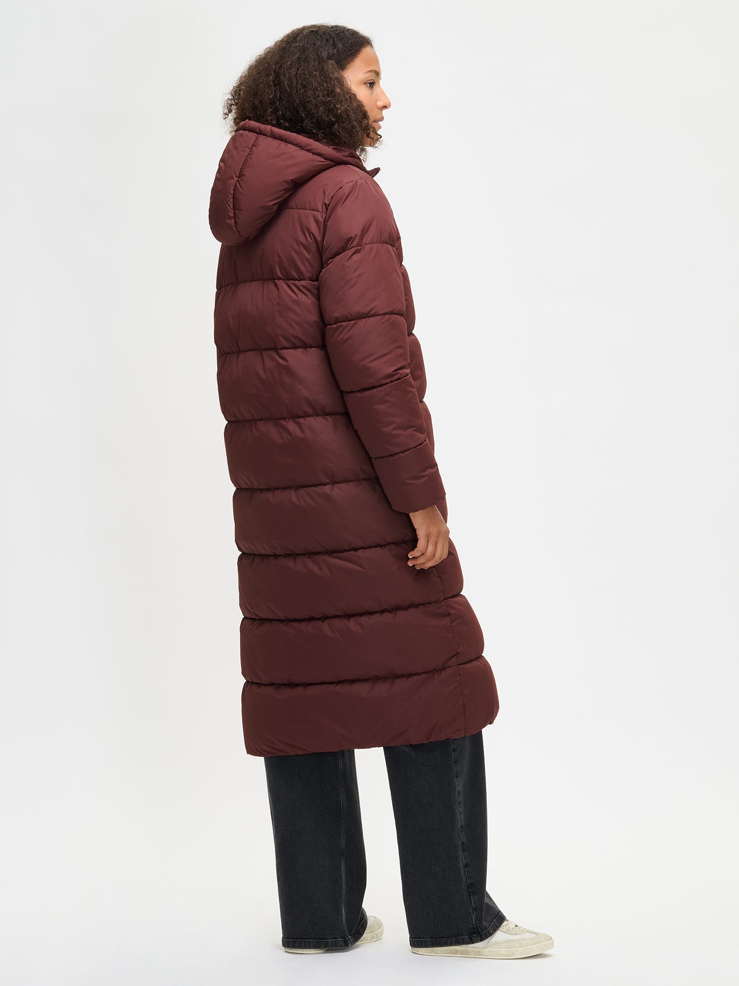 The Lumi Long Pink Puffer Coat in beige offers cozy warmth with its lightweight, puffy insulation. Worn by a model from the side.