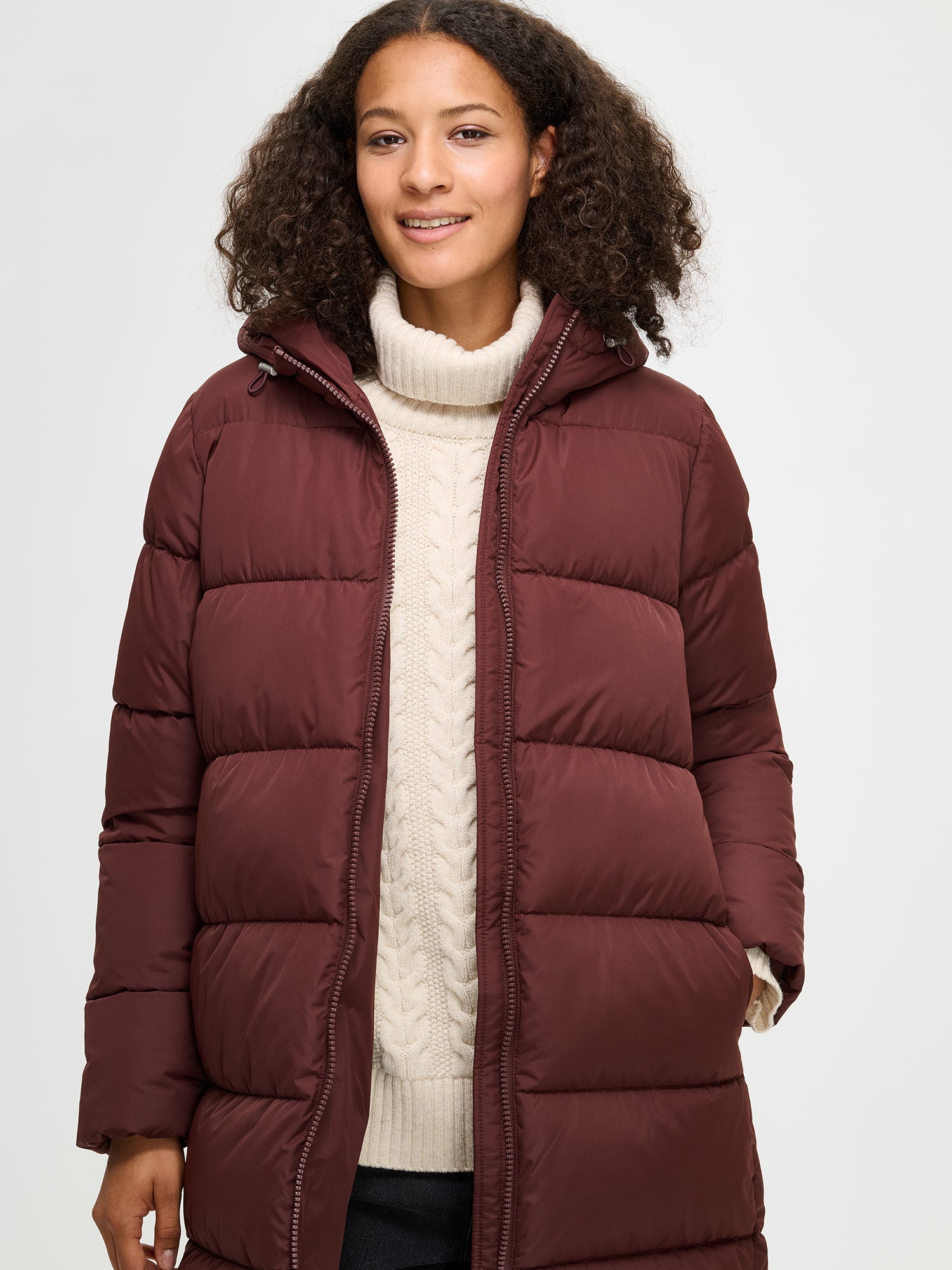 The Lumi Long Pink Puffer Coat in beige offers cozy warmth with its lightweight, puffy insulation. Worn by a model.
