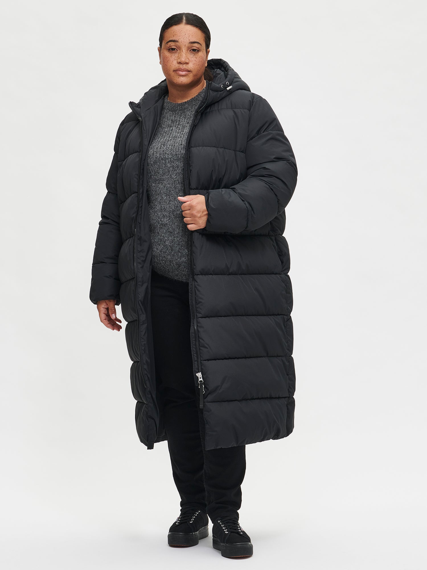 The Lumi Long Pink Puffer Coat in black offers cozy warmth with its lightweight, puffy insulation. Worn by a model with jacket open.