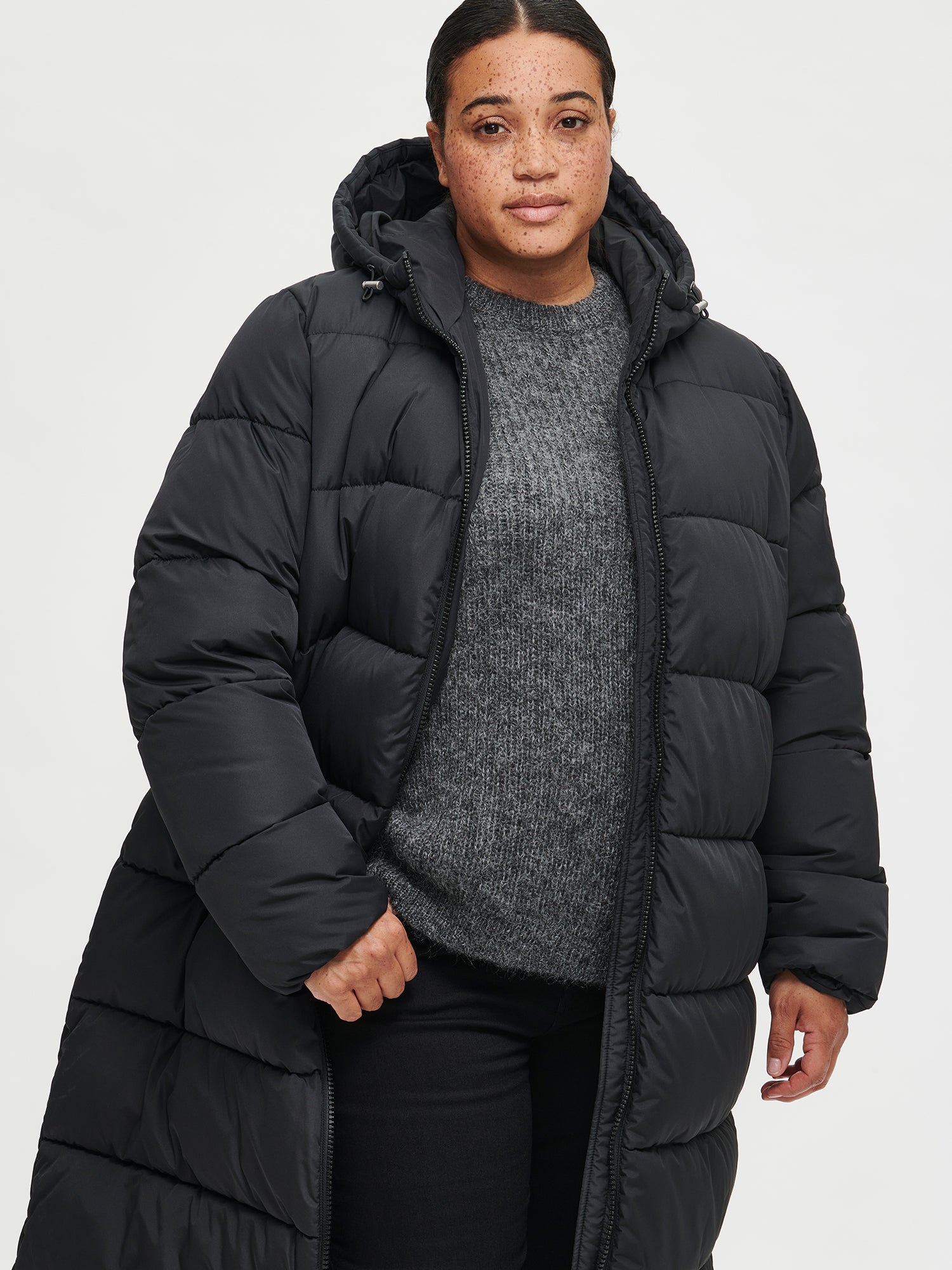 The Lumi Long Pink Puffer Coat in black offers cozy warmth with its lightweight, puffy insulation. Jacket open.