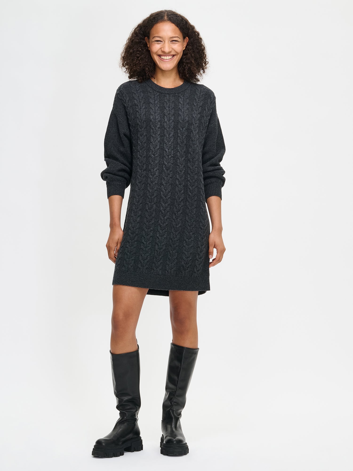 Woman wearing a dark gray cable knit dress with black knee-high boots on a white background