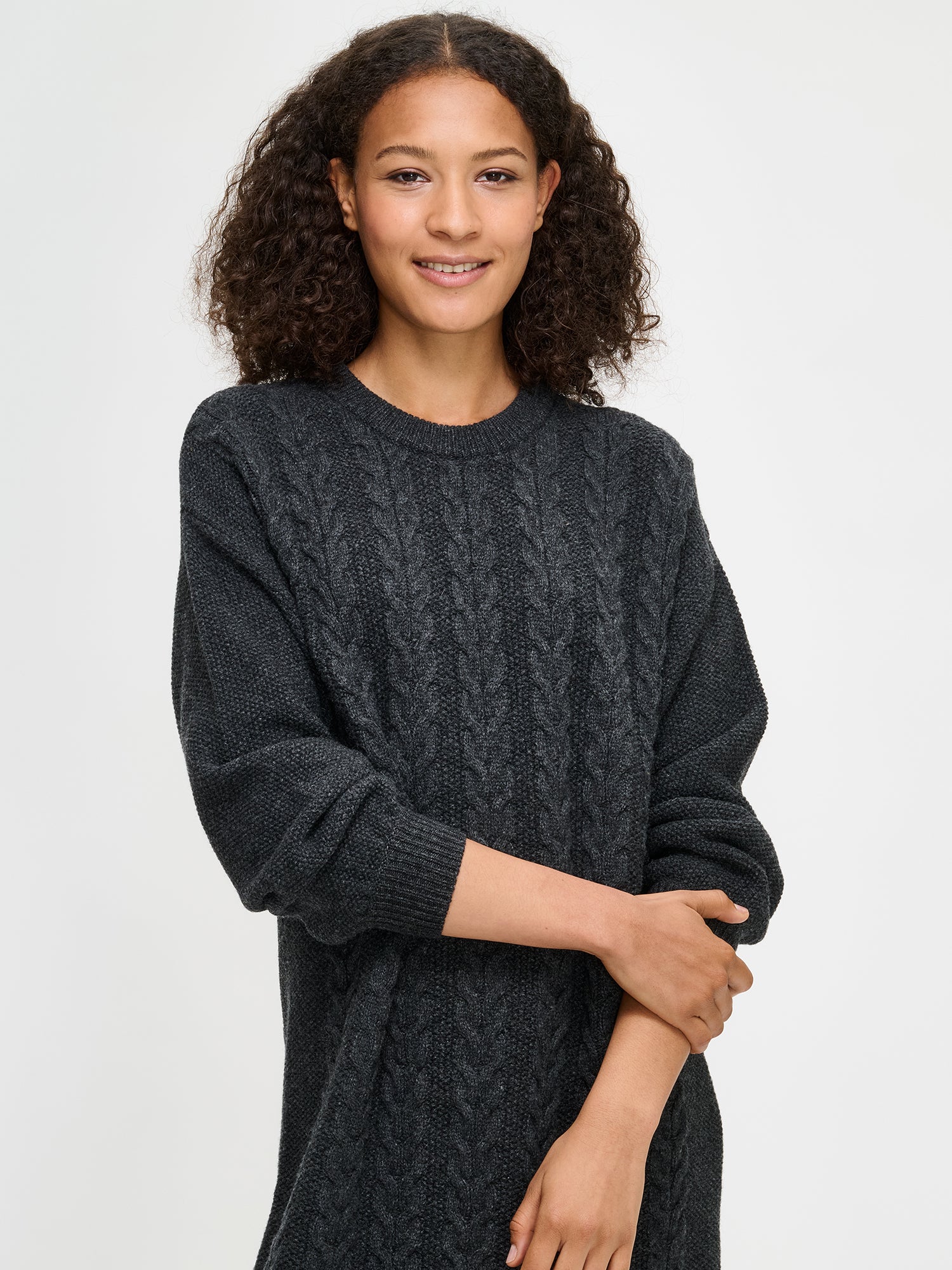 Woman wearing a dark gray cable knit sweater against a white background
