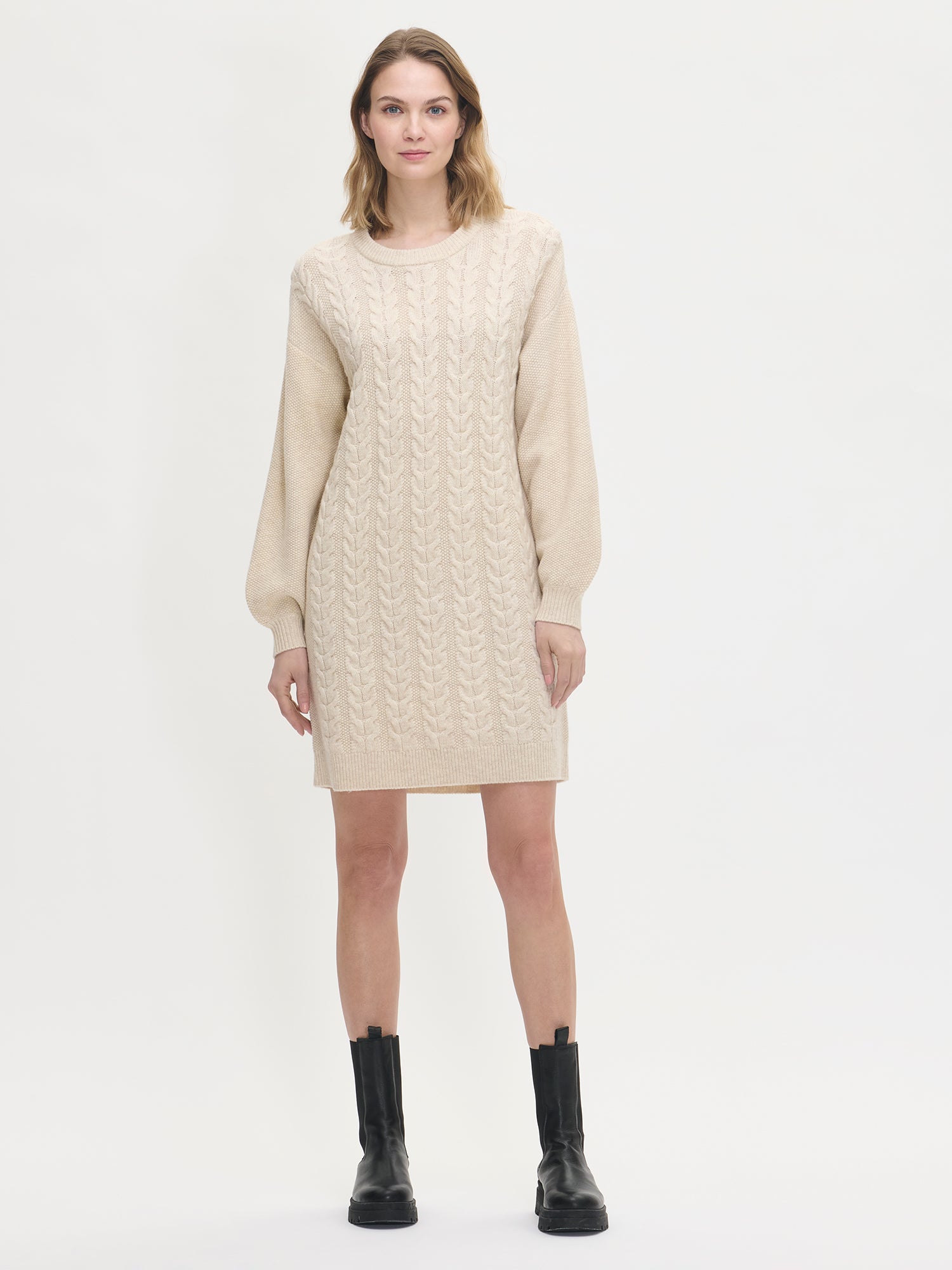Woman wearing a beige cable knit dress on a white background