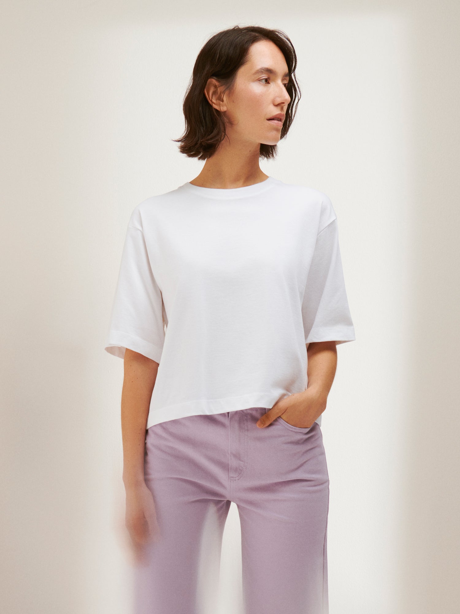 Nanso women's solid white Forma T-shirt. This boxy, loose-fitting T-shirt features a round ribbed neckline and loose 2/4-length sleeves. On a model with jeans.