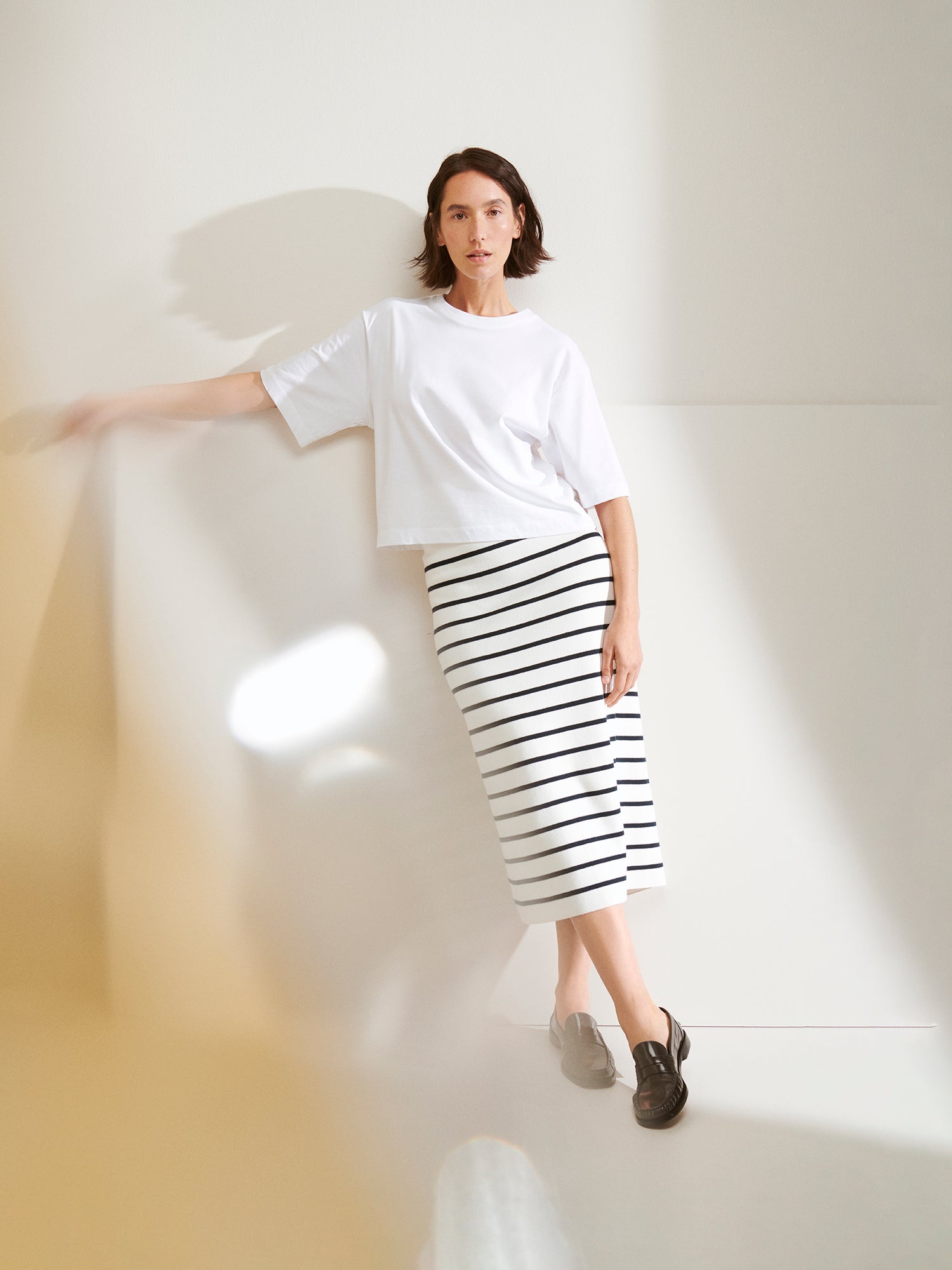 Nanso women's solid white Forma T-shirt. This boxy, loose-fitting T-shirt features a round ribbed neckline and loose 2/4-length sleeves. On a model with skirt.