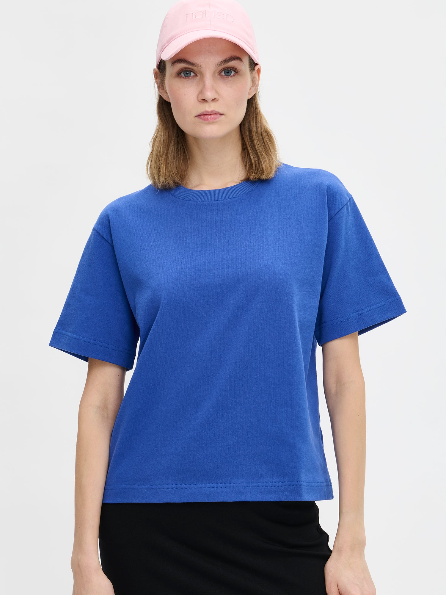 Nanso women's solid blue Forma T-shirt. This boxy, loose-fitting T-shirt features a round ribbed neckline and loose 2/4-length sleeves. On a model with a midi skirt and cap, close-up.