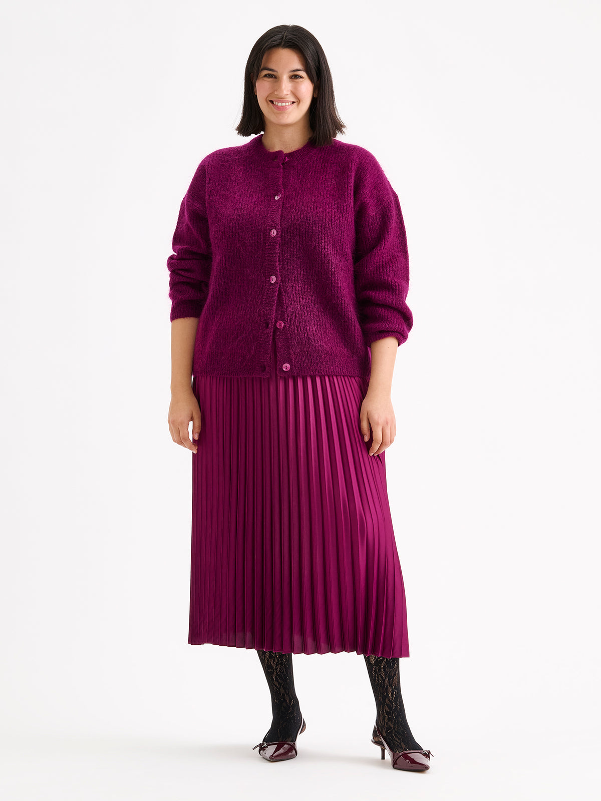 Nanso's elegant Taite skirt for women features a graceful drape in a vibrant violet shade, on a model with a violet sweater.