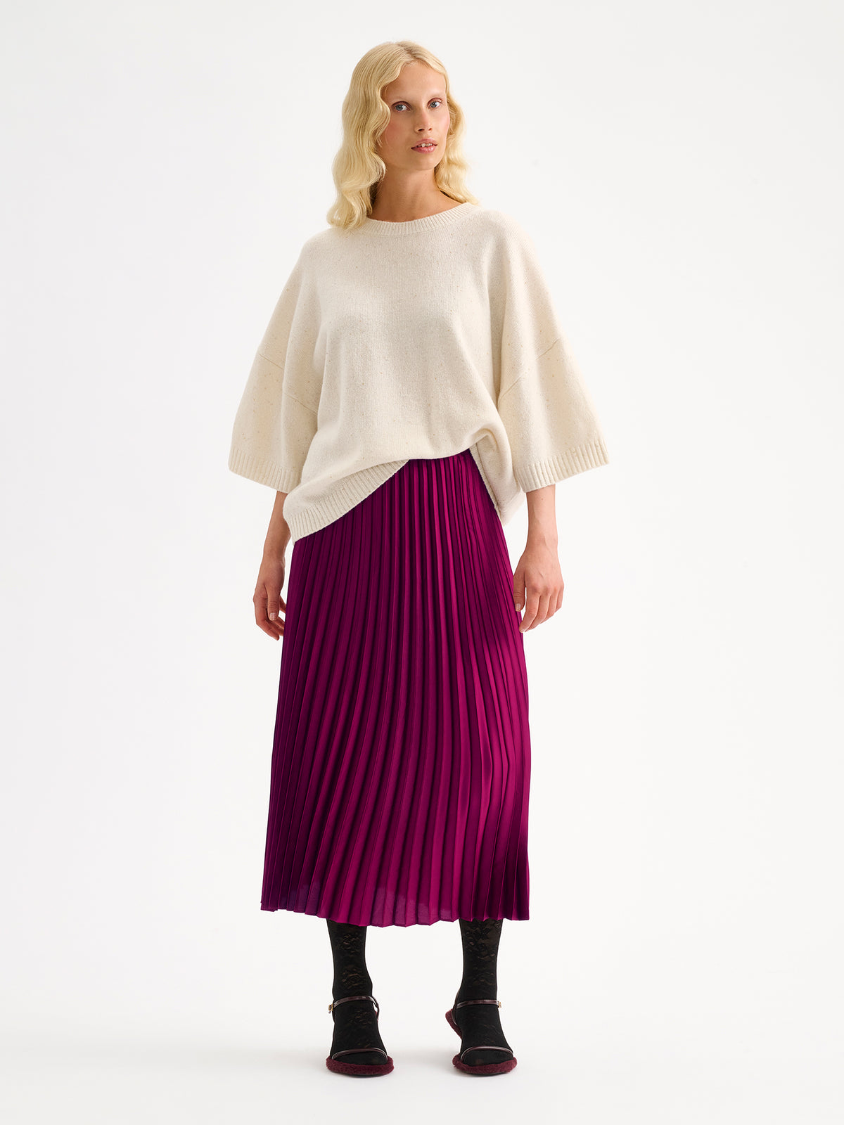 Nanso's elegant Taite skirt for women features a graceful drape in a vibrant violet shade, on a model with a white half-sleeved sweater.