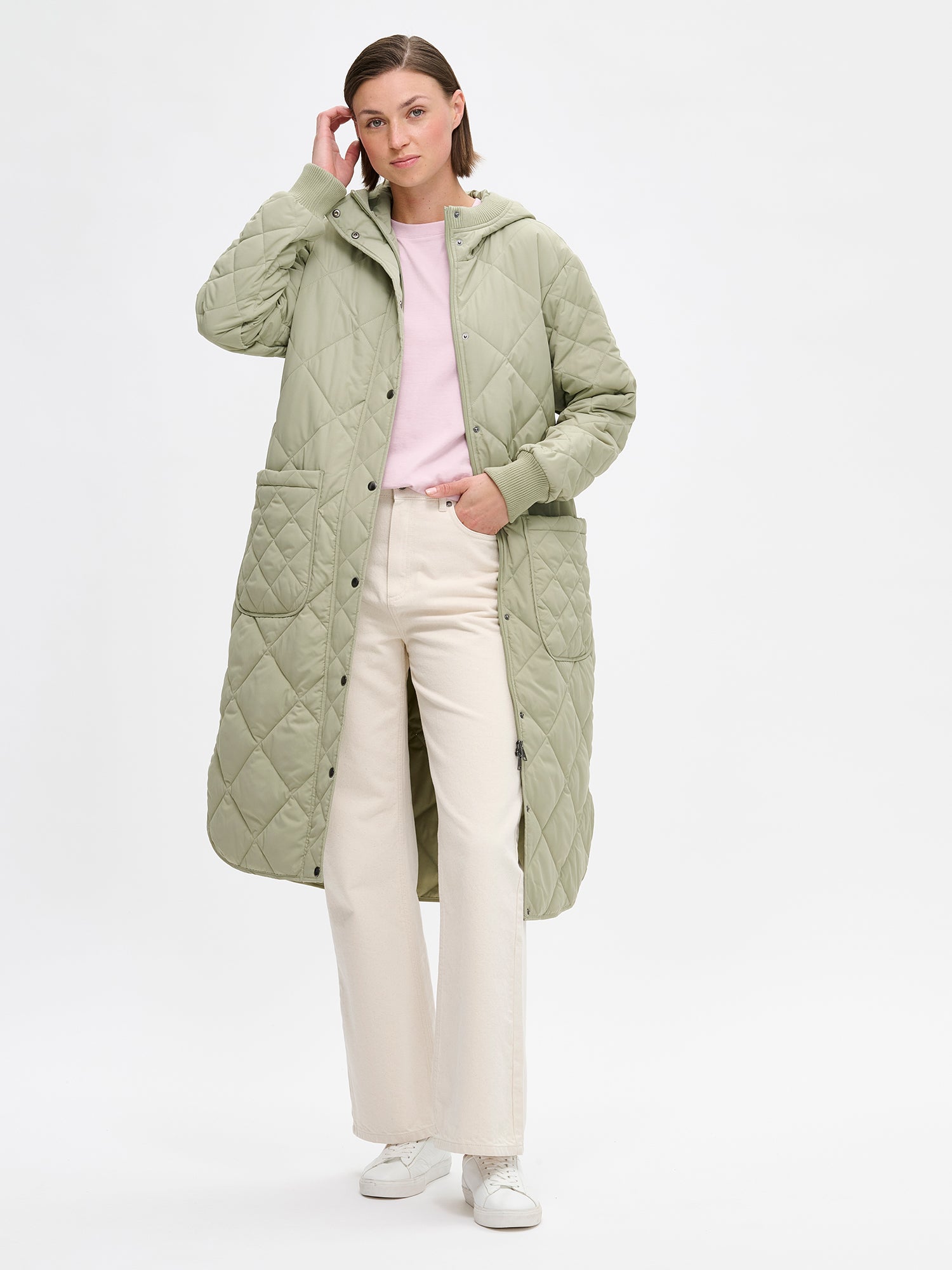 Nanso women's casual green Maxi quilted coat with light padding and a cozy hood. Perfect for in-between seasons, the hooded jacket features a two-way front zipper with a snap-button wind flap, a comfortable ribbed hood edge and cuffs. On a model with the coat opened.