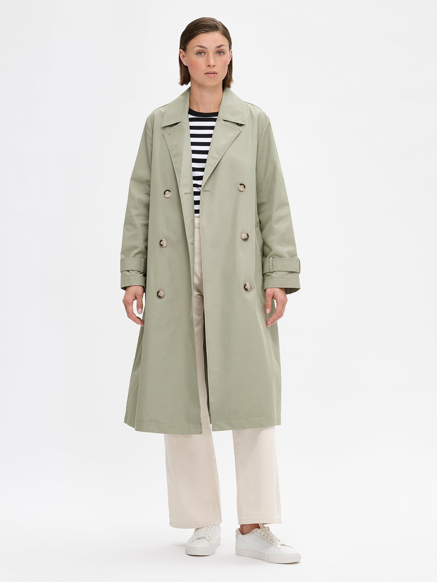 A timeless Light Green trench coat on a model with off white jeans.