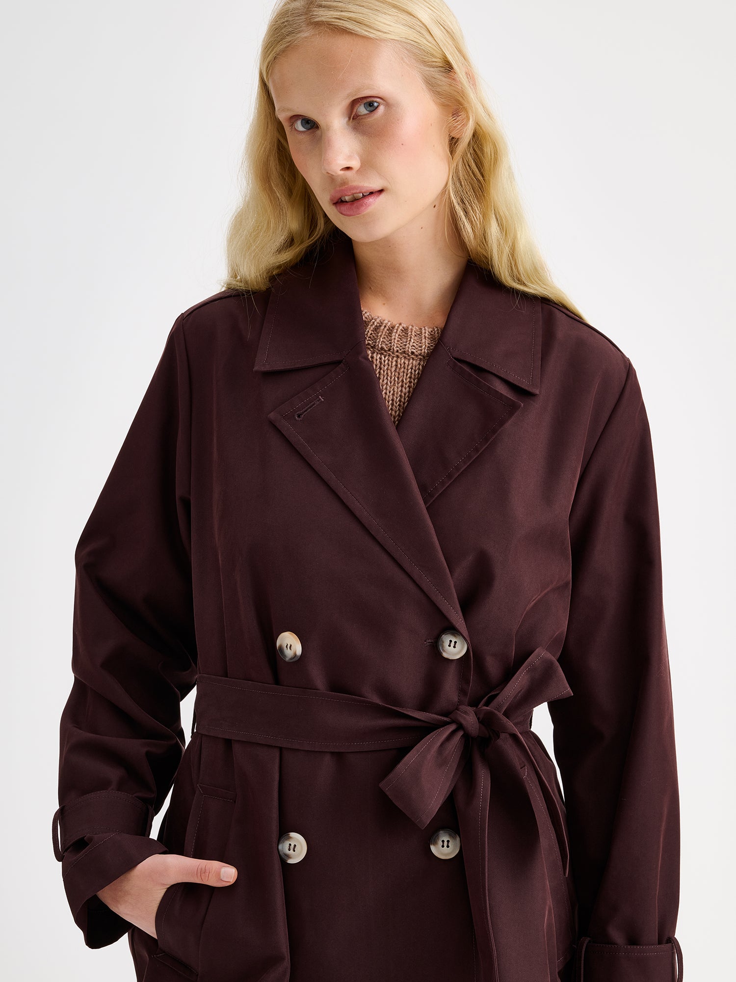 A timeless Brown trench coat on a blonde model, close-up.