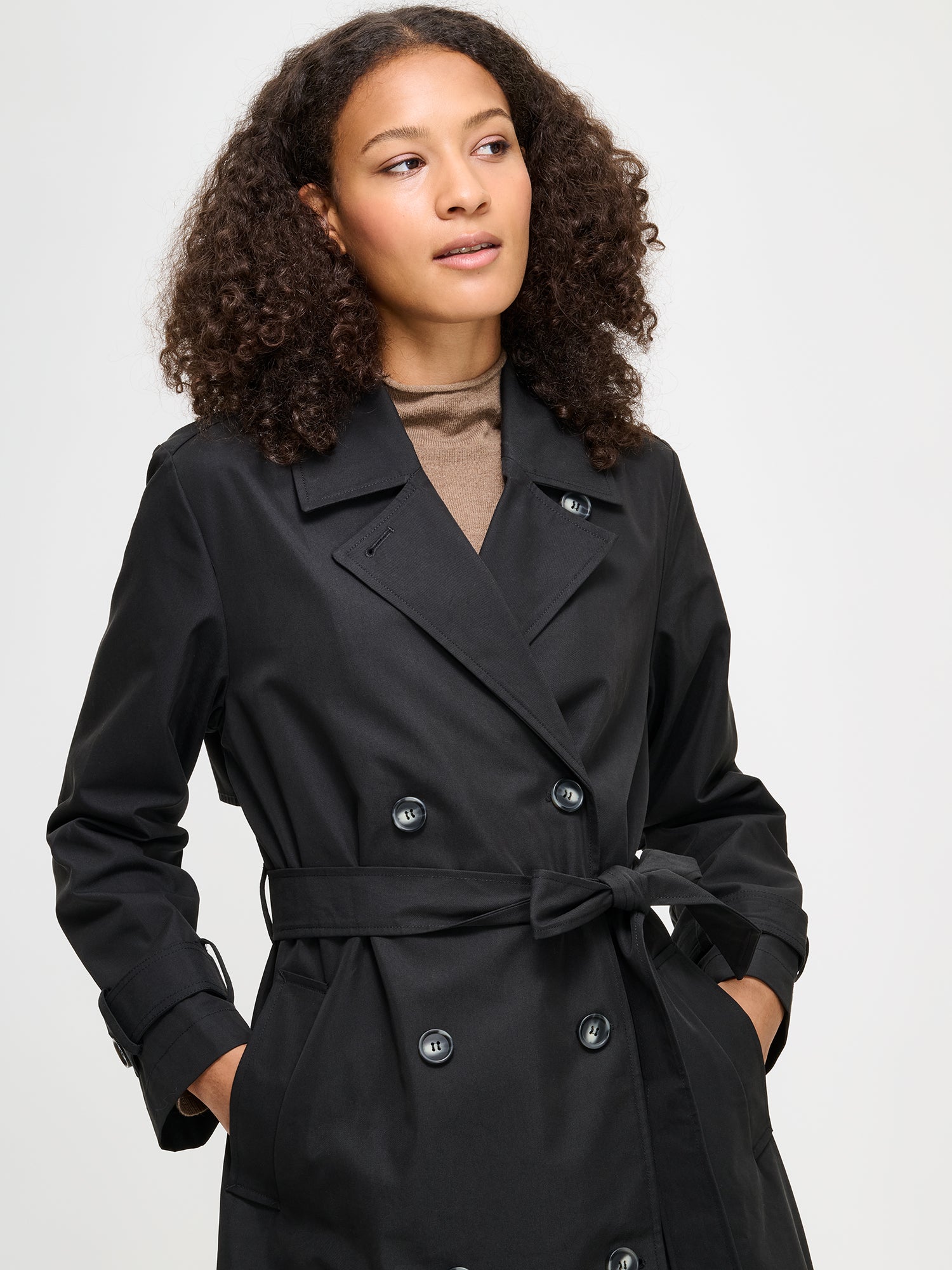 Woman wearing a black trench coat on a plain background