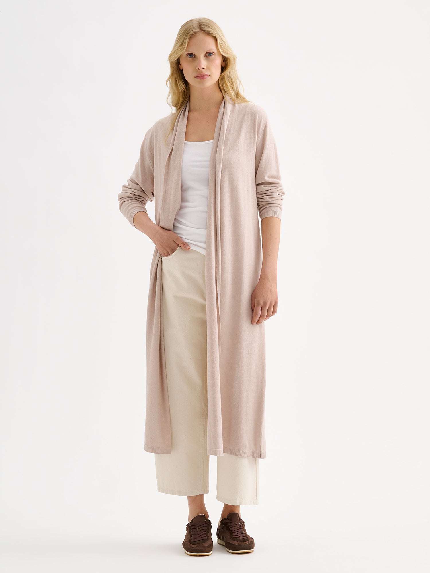 Nanso women's elegant long Karina cardigan in soft and neutral light beige on a model with natural white jeans and a white top.