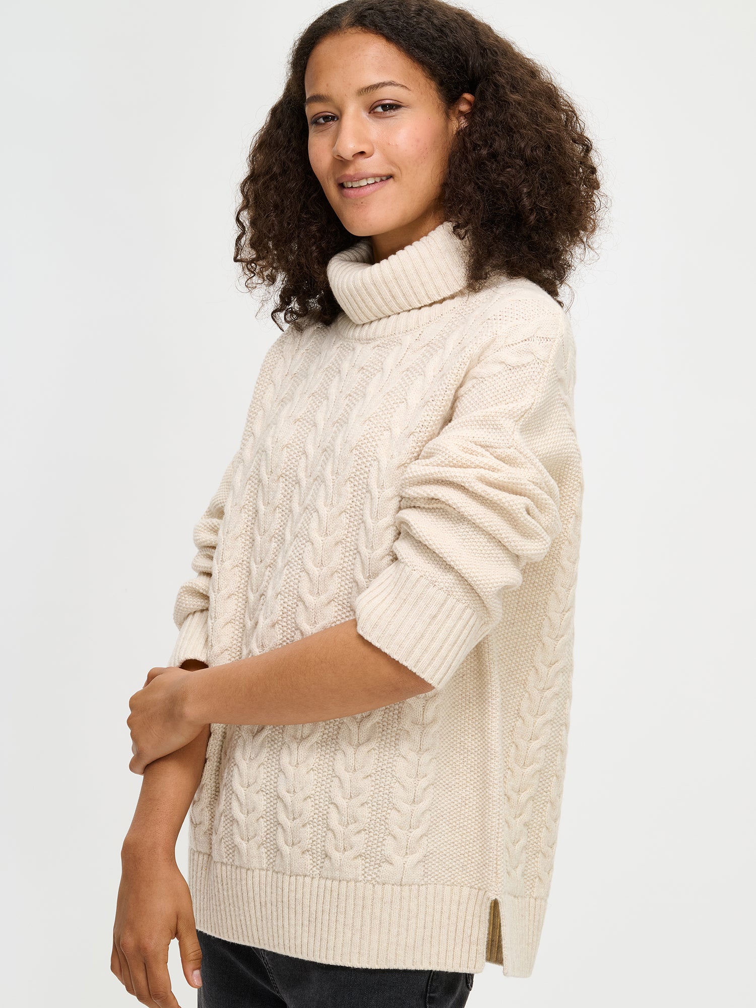 Woman wearing a cream cable knit sweater on a white background