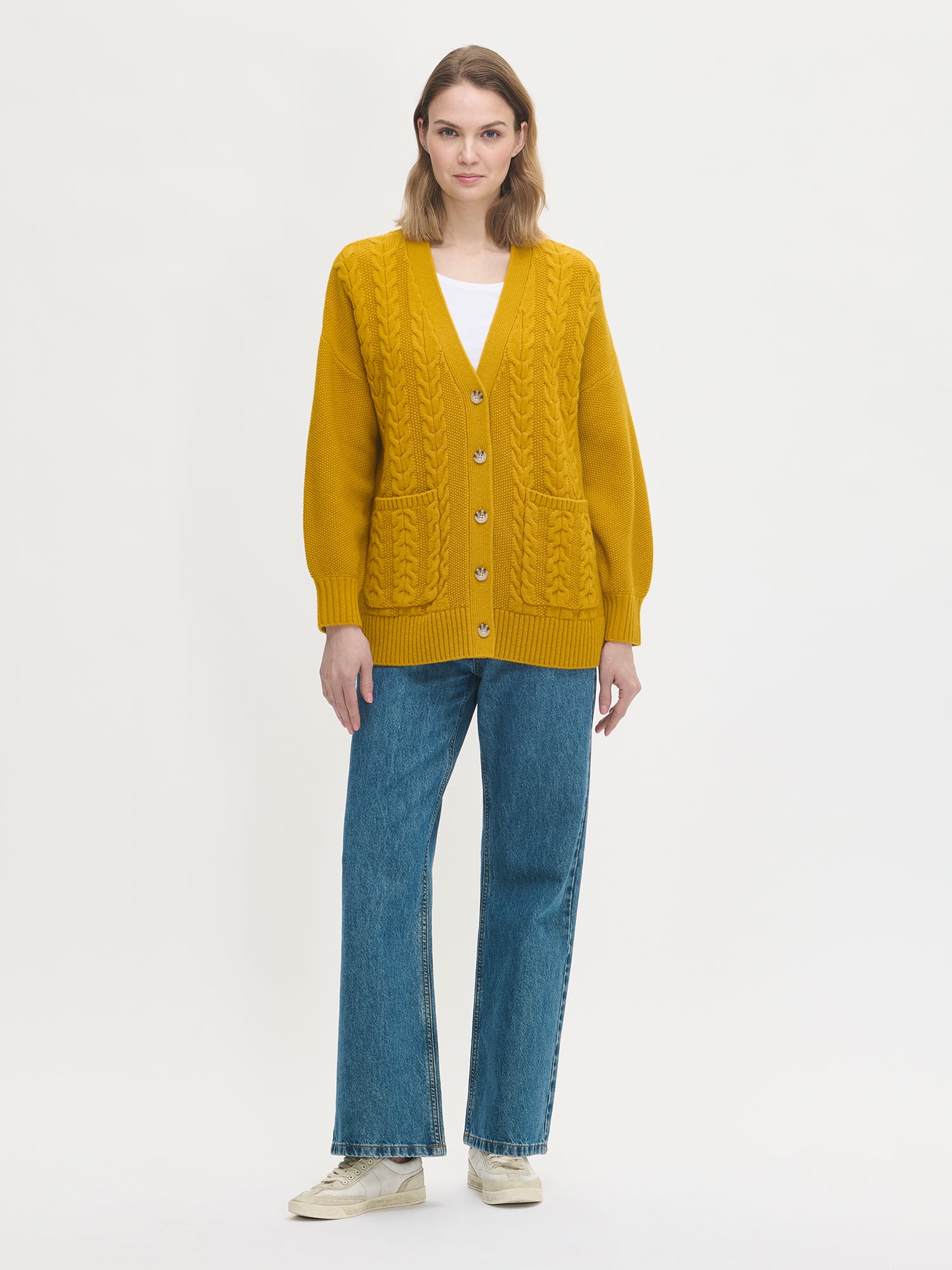 Woman wearing a yellow cardigan and blue jeans on a white background