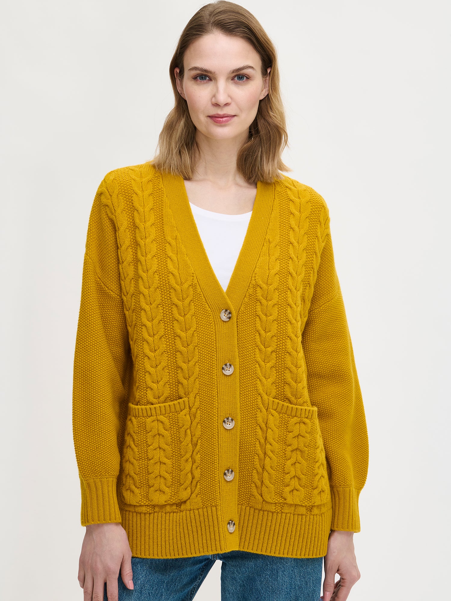 Woman wearing a yellow cable knit cardigan on a white background