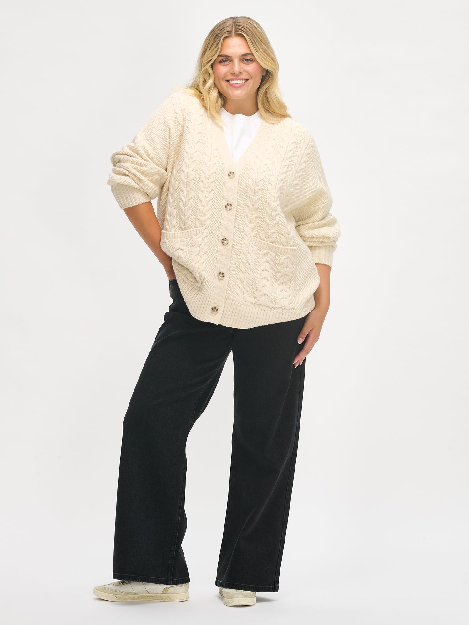 Woman wearing a beige cardigan and black pants on a white background