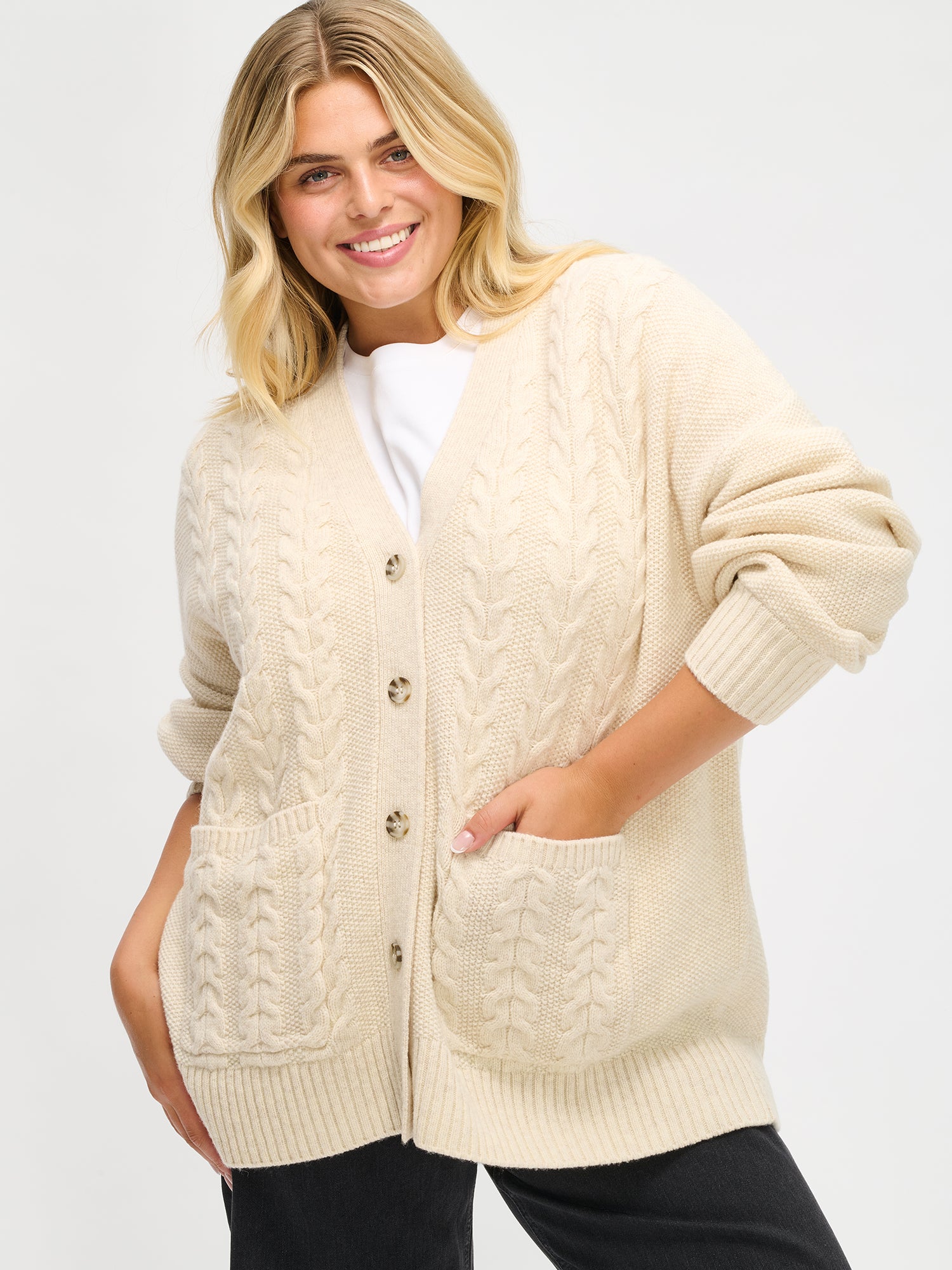 Woman wearing a cream cable knit cardigan on a white background