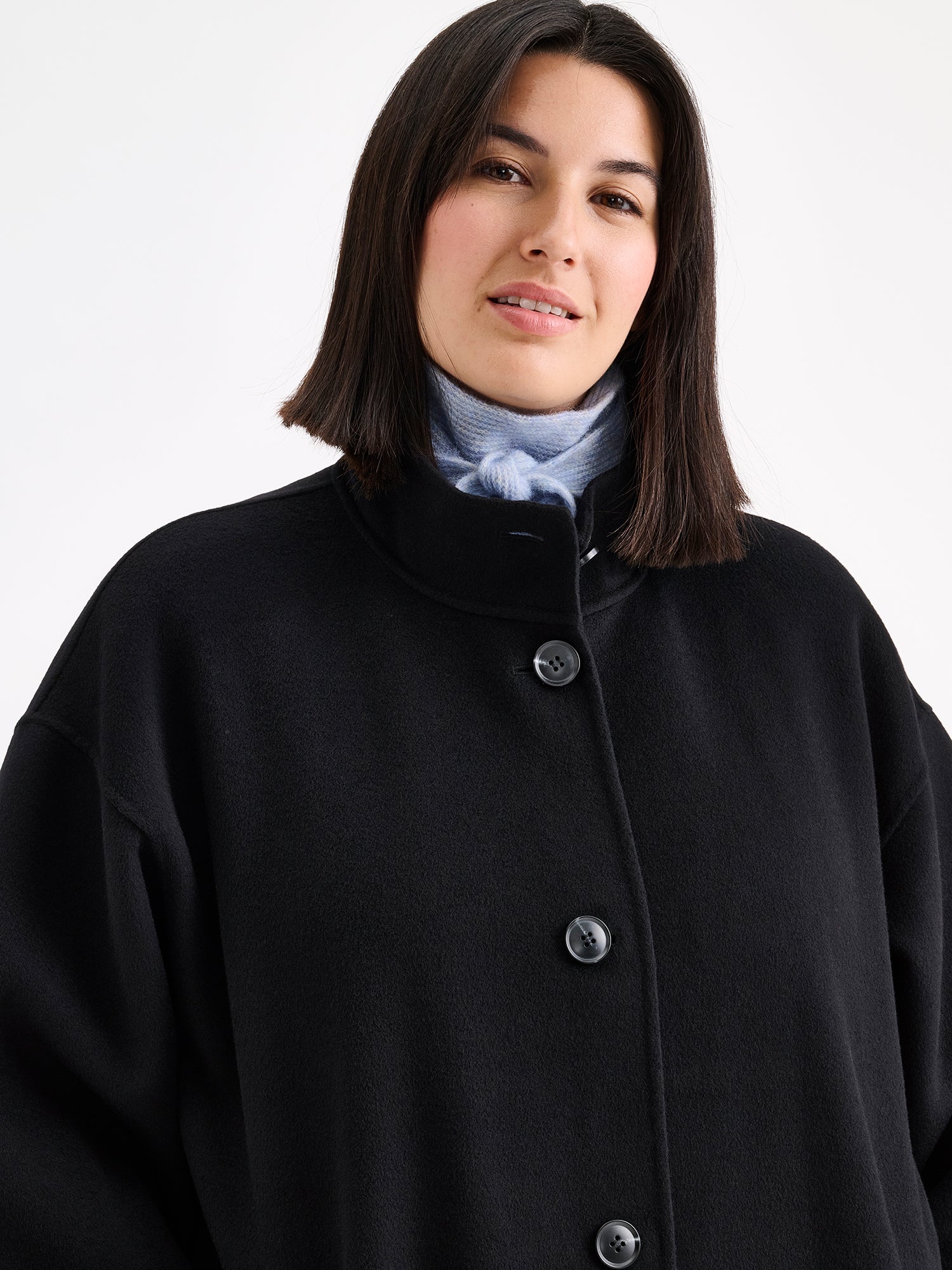 Nanso women's long black Elle wool coat on a brunette model with a light blue scarf. | XL - 178cm
