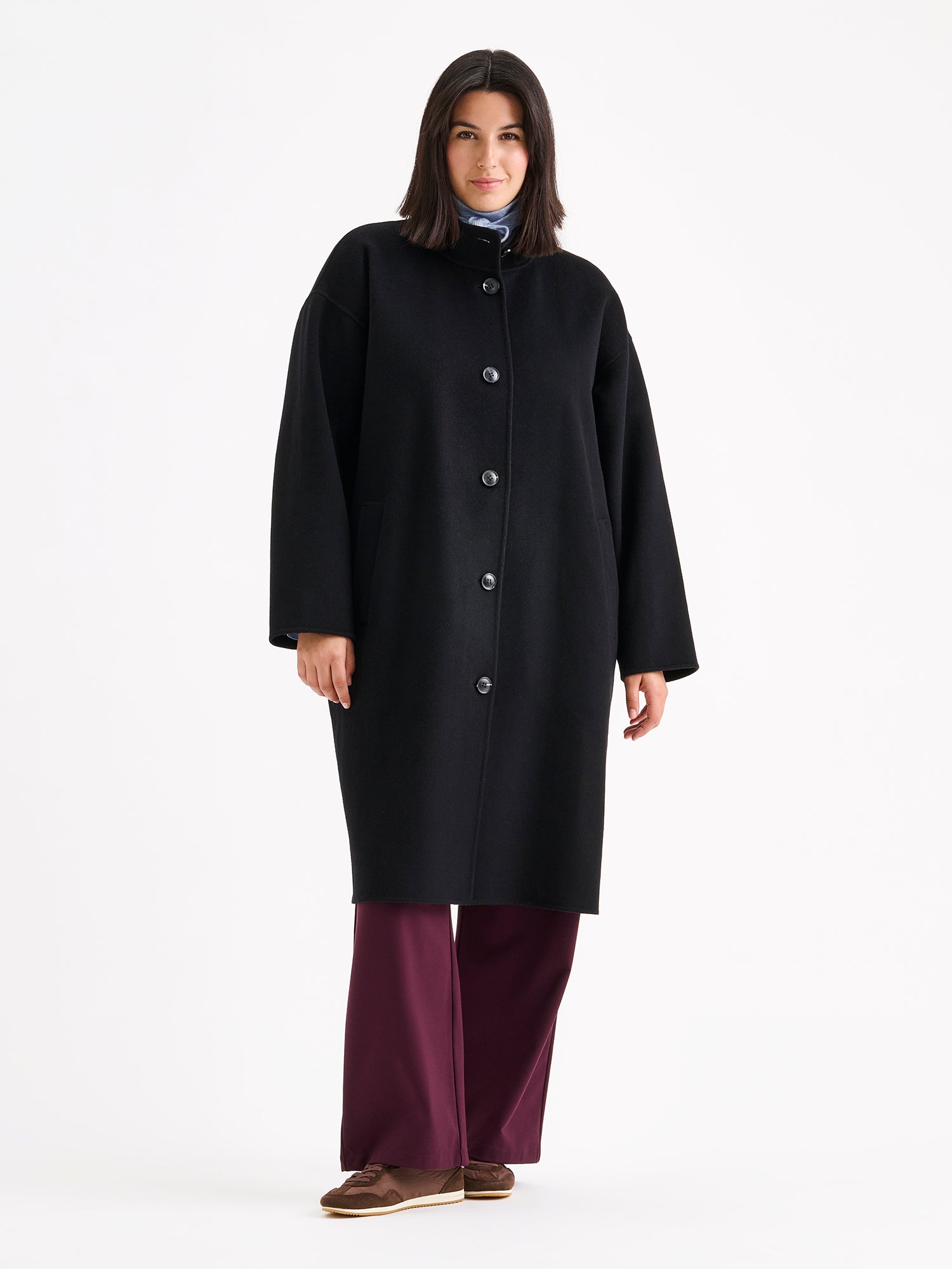Nanso women's long black Elle wool coat on a brunette model with a light blue scarf and winered jeans.