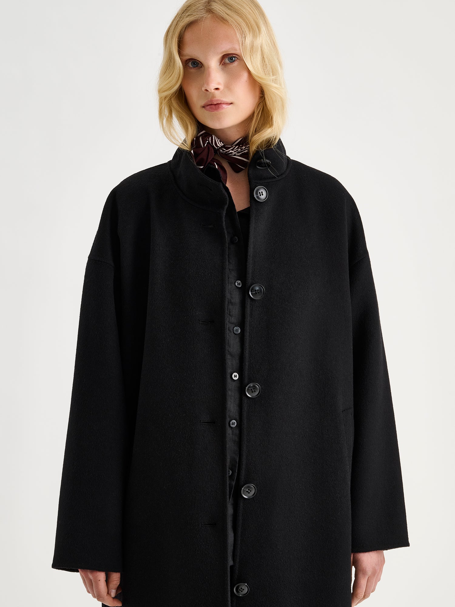 Nanso women's long black Elle wool coat on a blonde model with a small scarf.