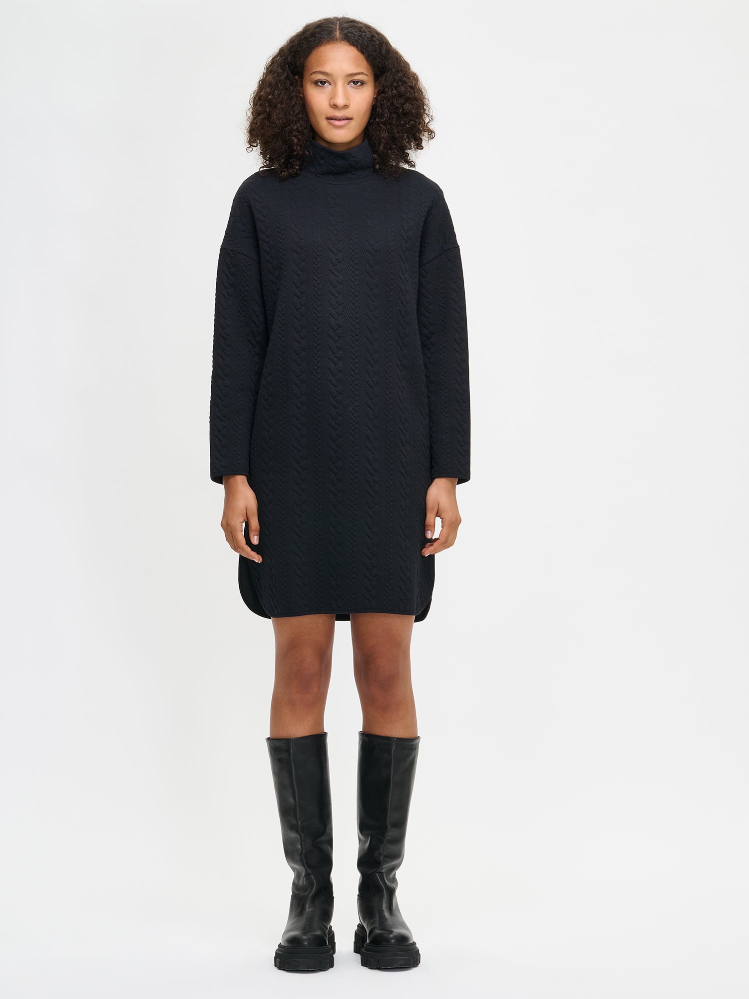 Woman wearing a black dress and black knee-high boots on a white background