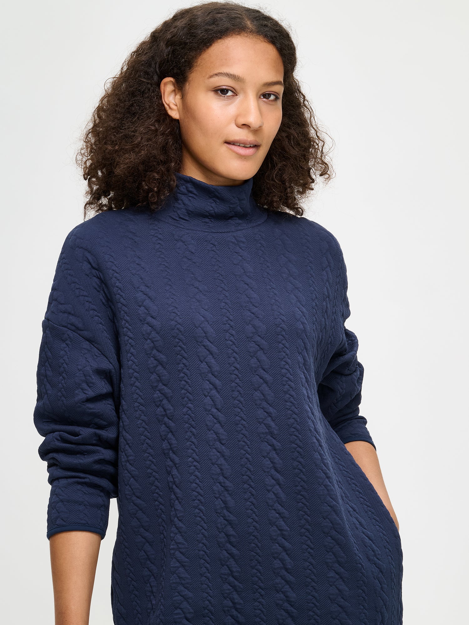 Woman wearing a dark blue dress with a turtleneck and black boots on a white background