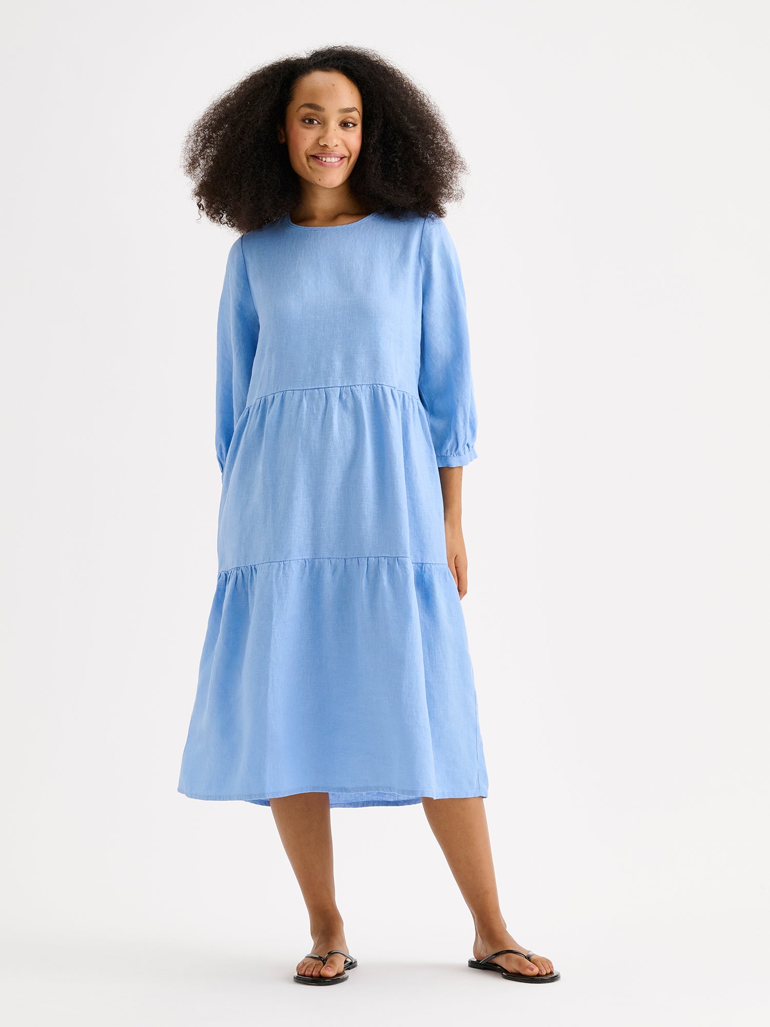Nanso women's Saralia Linen Dress in blue with voluminous frill layers on a model with flip flops.