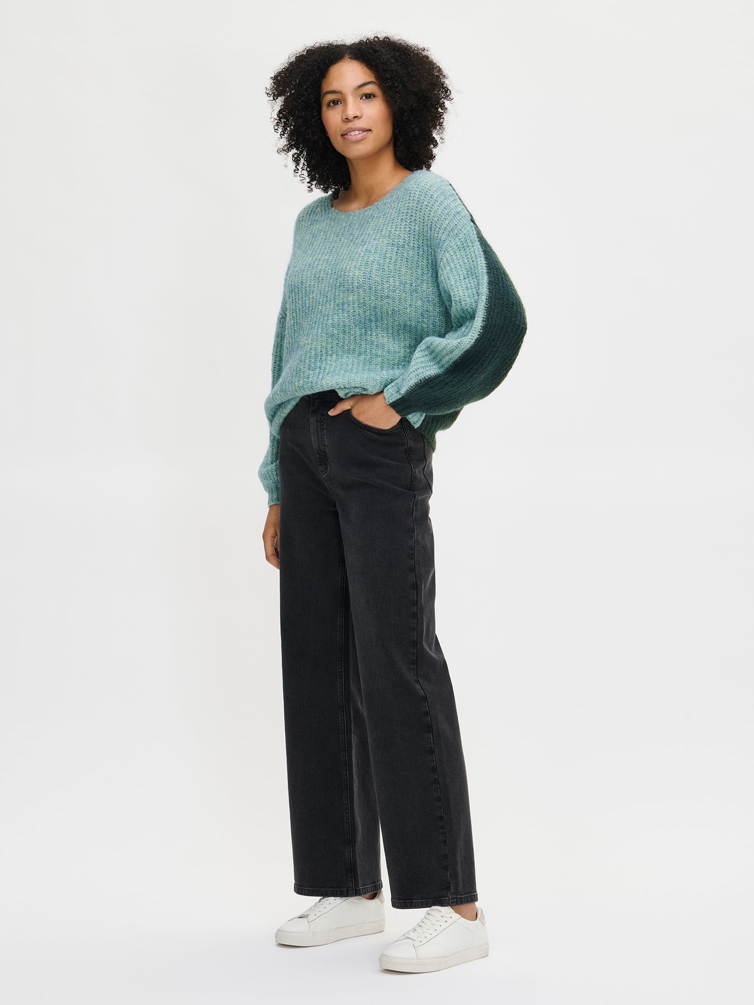 Nanso Women's luxurious green Karamelli knit sweater with contrasting green colors, on a model with jeans from the front.