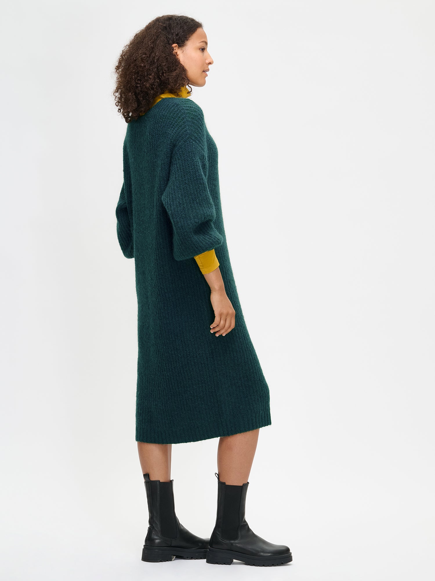 Woman wearing green Karamelli knit dress with yellow sleeves and black boots
