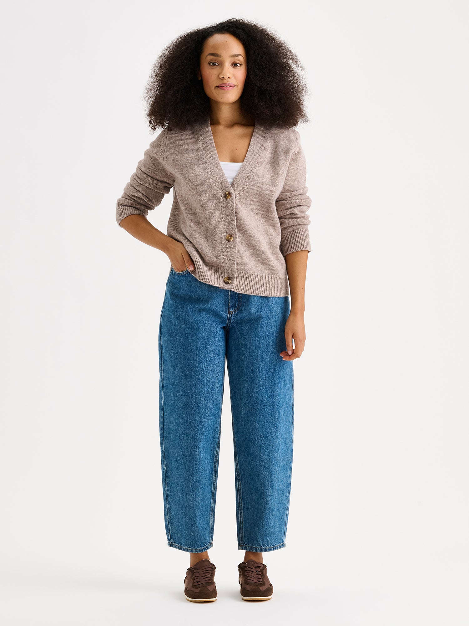 The LANA long-sleeved Knit Cardigan in greige with a flattering V-neckline and button closure down the front. On a model with jeans.