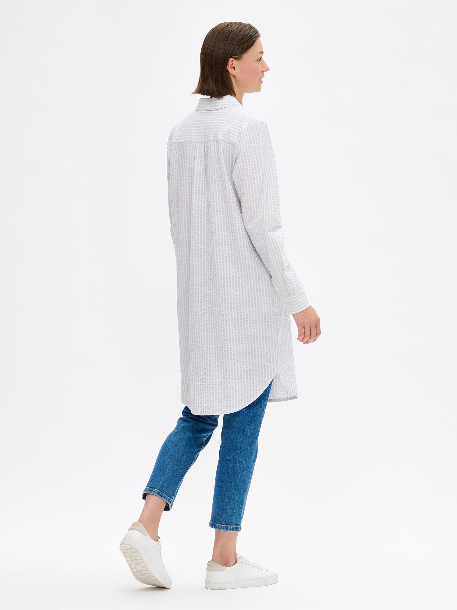 Nanso women's MAREA shirt dress in pale blue features a classic collar, front button closure, rounded hemline. A chest pocket and side pockets add everyday functionality. On a model pictured from the back.