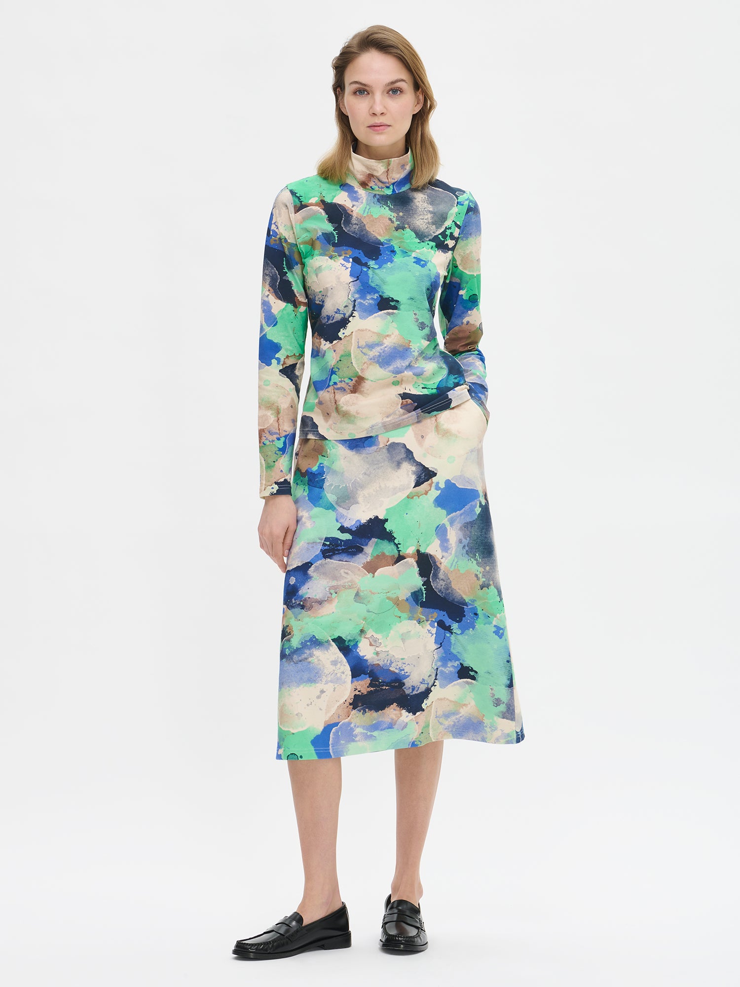 The SIRIUS Shirt features a beautiful abstract pattern paired with a classic turtleneck collar, made from organic cotton-elastane knit fabric. On a model from the front.