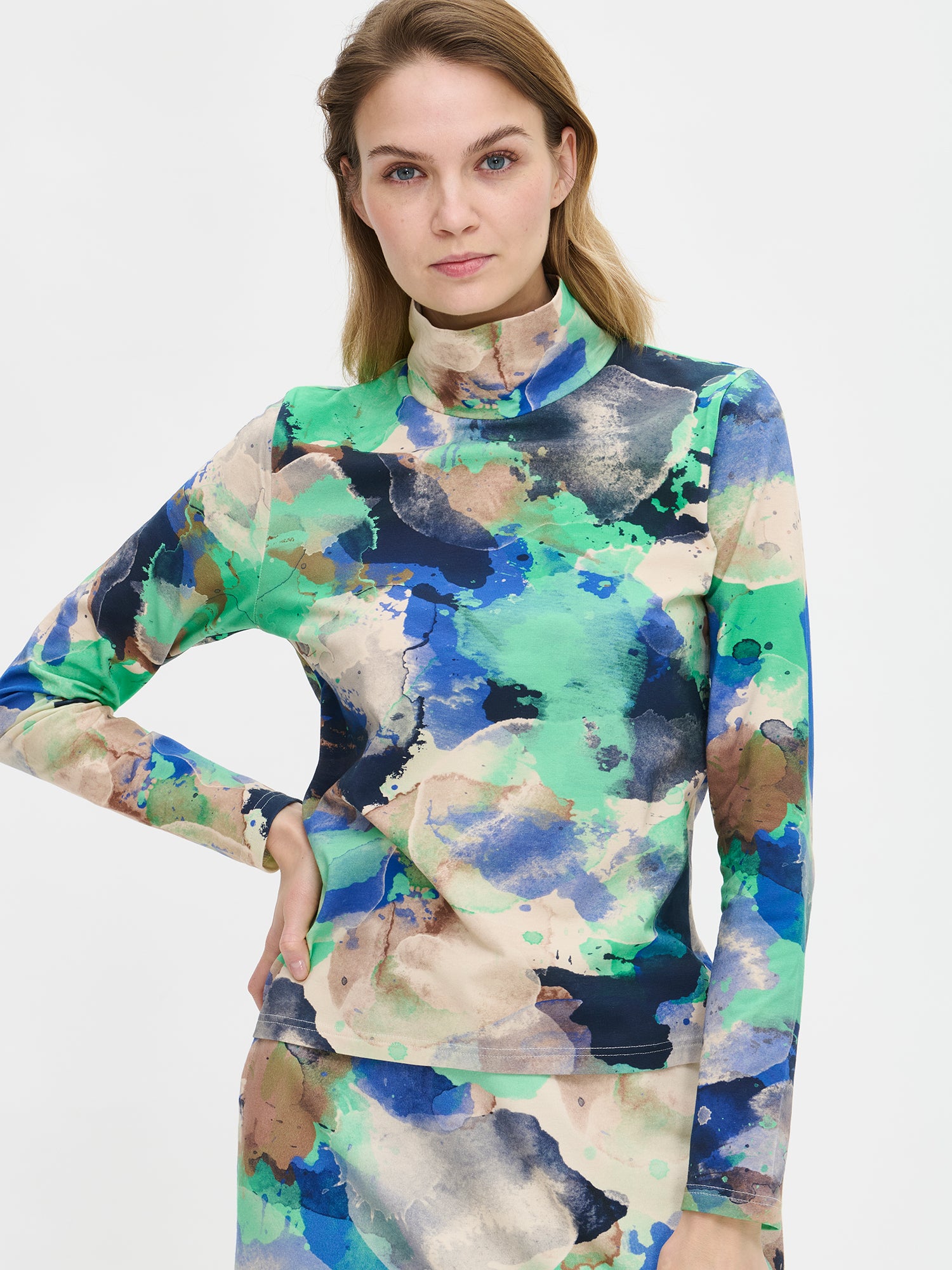 The SIRIUS Shirt features a beautiful abstract pattern paired with a classic turtleneck collar, made from organic cotton-elastane knit fabric. On a model from the front, close-up.