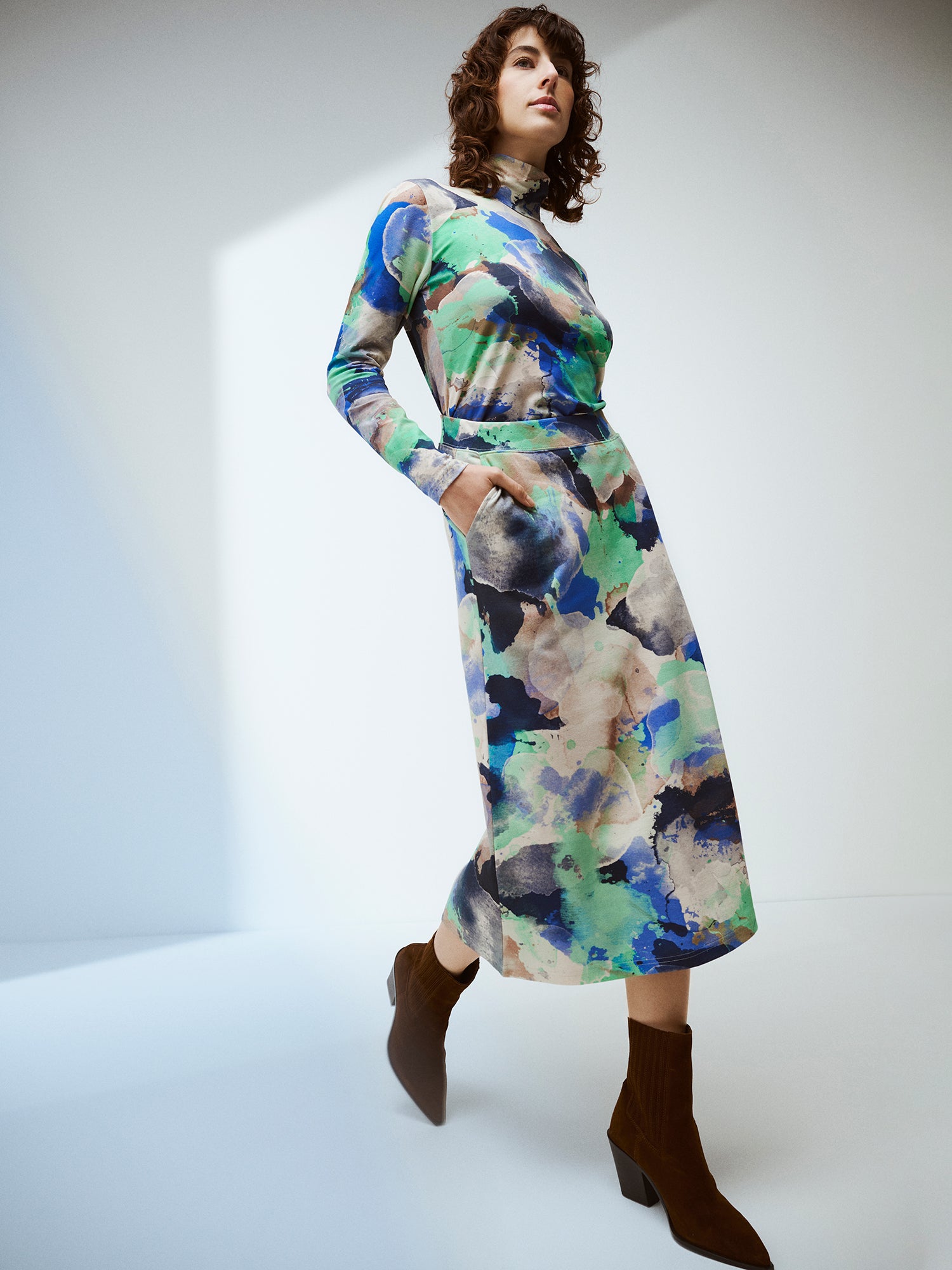 The SIRIUS Shirt features a beautiful abstract pattern paired with a classic turtleneck collar, made from organic cotton-elastane knit fabric. On a model with a matching skirt and boots in brand picture.